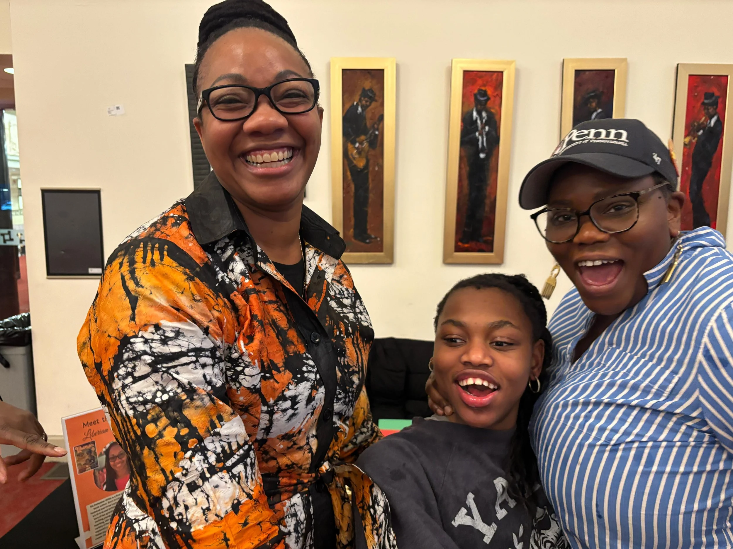 Group of smiling people at an art gallery, with paintings of musicians in the background.