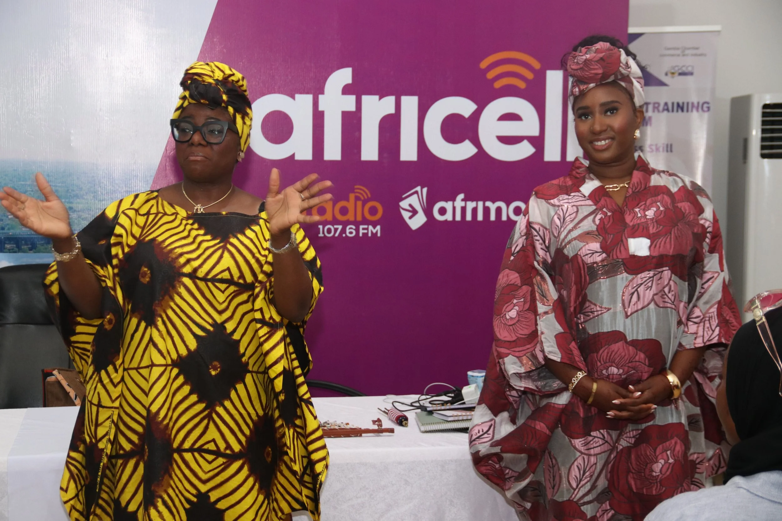 Two women wearing traditional African attire and headwraps, standing in front of a purple background with the text 'african radio 107.6 FM'.