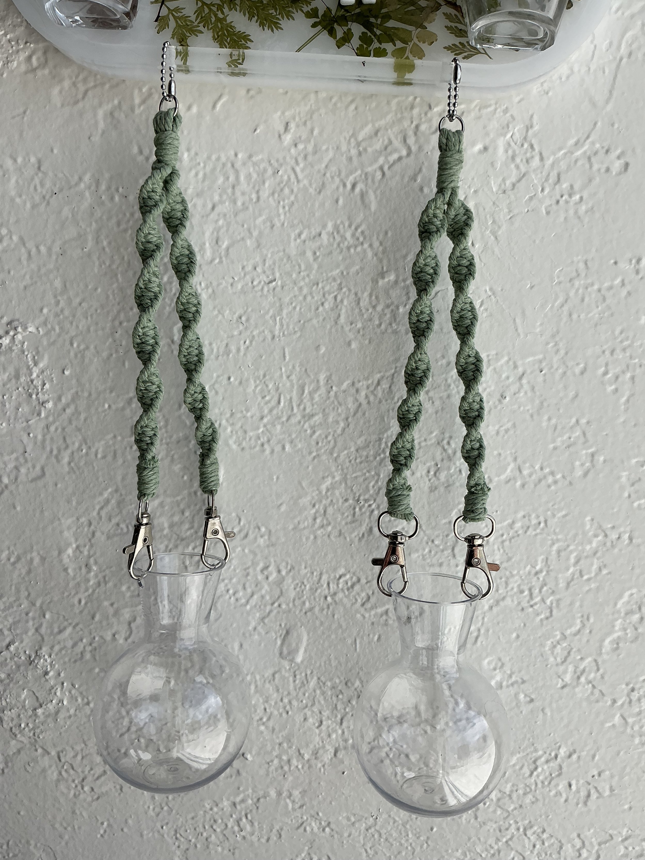 Close view of the two lower round propagation vases hanging from sage green knotted macramé, with silver lobster clasps and attachment rings visible.