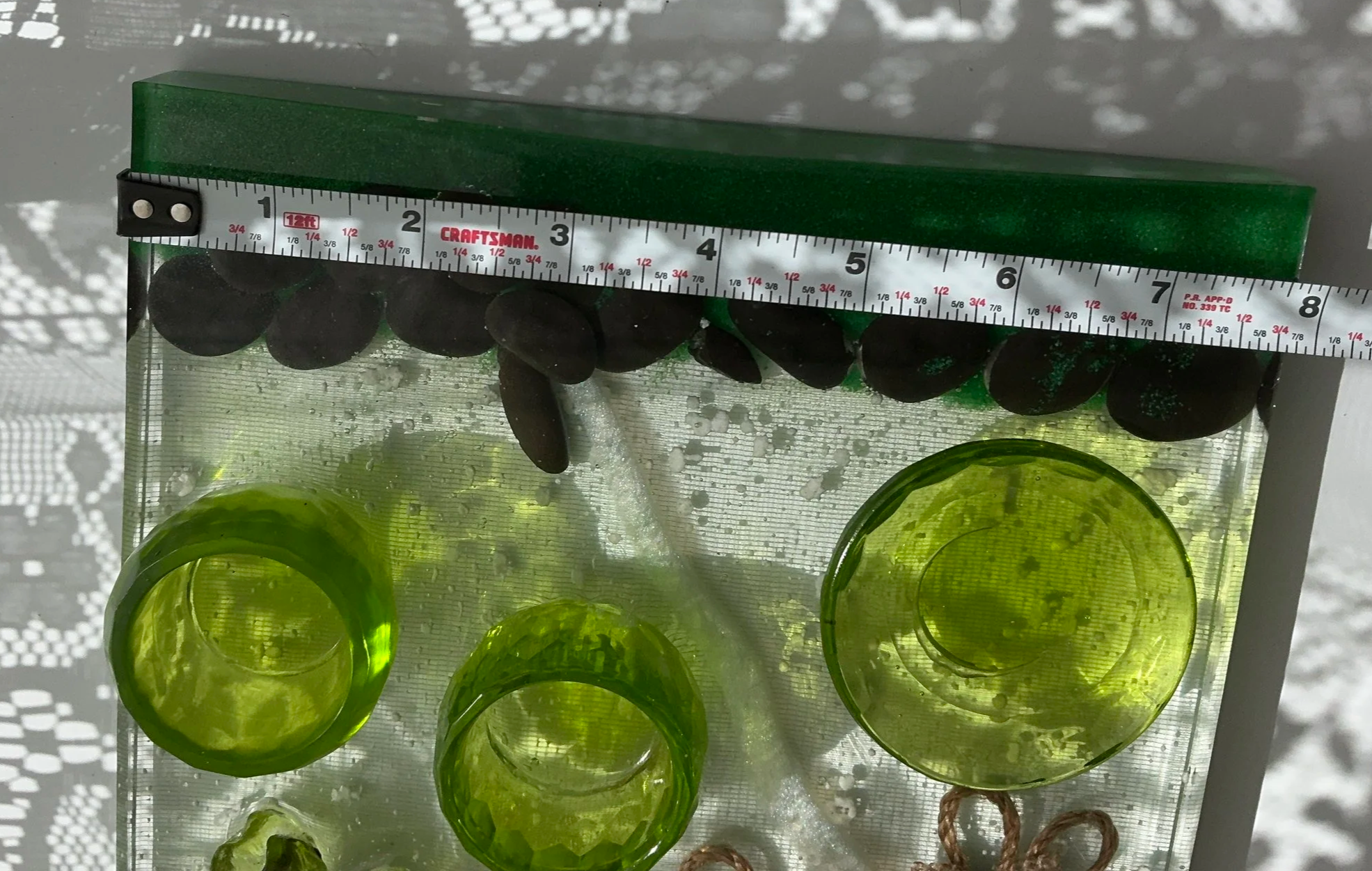 Measuring tape across the clear resin propagation station shows its approximately 8-inch width, providing scale for the glass vase, two green plant holders and embedded botanical decorations.