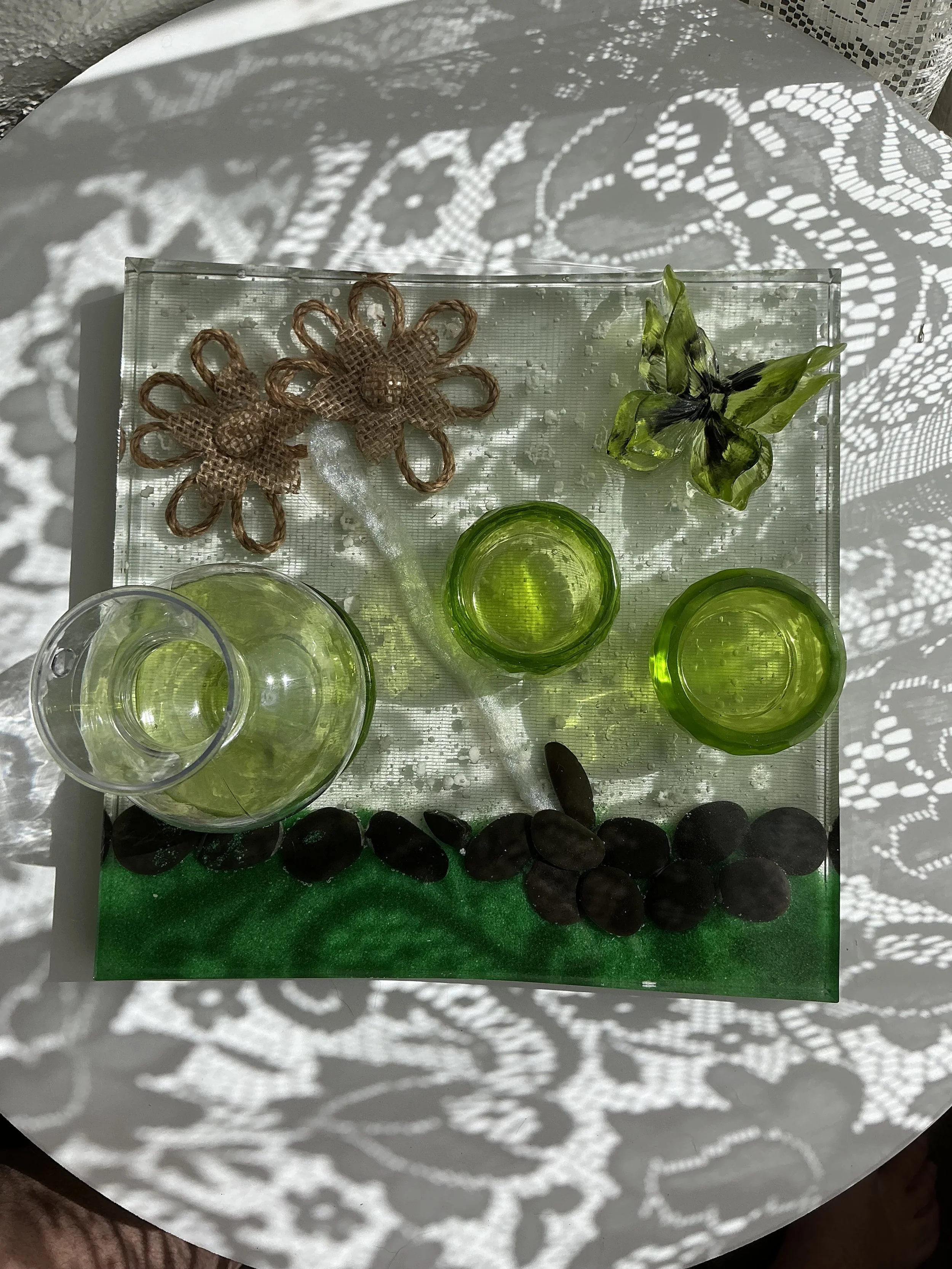 Overhead detail of smooth black stones nestled along the emerald green resin border. Sunlight brings out the shimmering color, transparent layers and natural variations in the handcrafted surface.