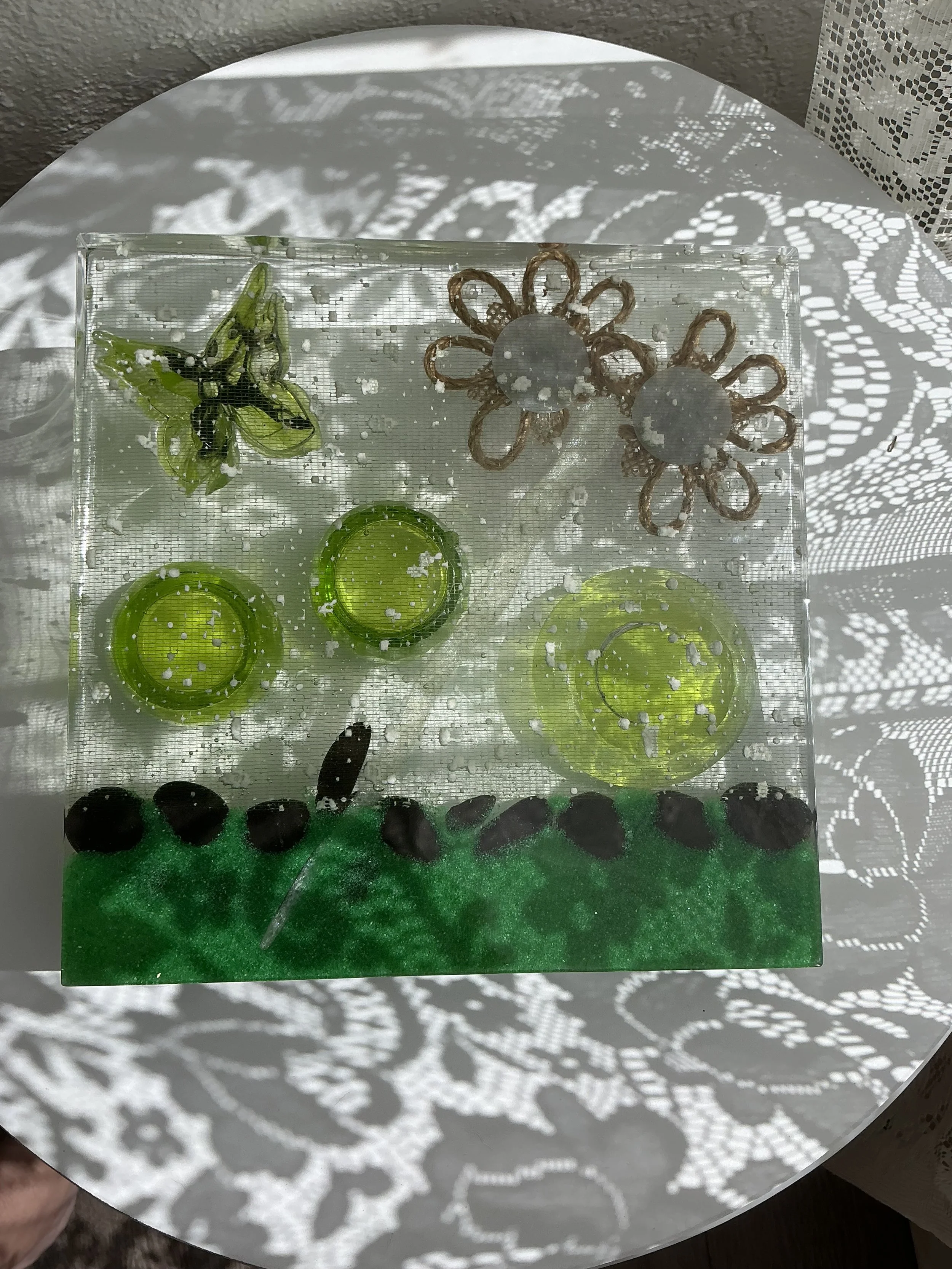 Reverse view of the square resin propagation station showing the green butterfly, burlap flowers, white branch and black stone border through the transparent base, revealing its layered construction.