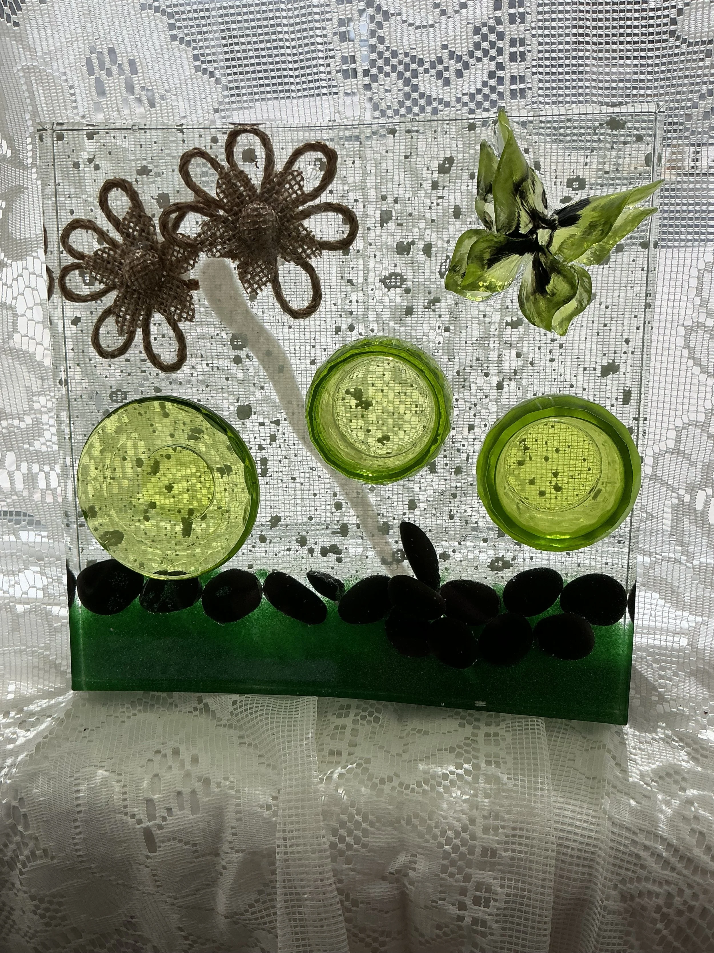 Front view of the clear resin botanical station against white lace. Light shines through the green vessels and butterfly, highlighting the embedded black stones and deep emerald garden-like border.