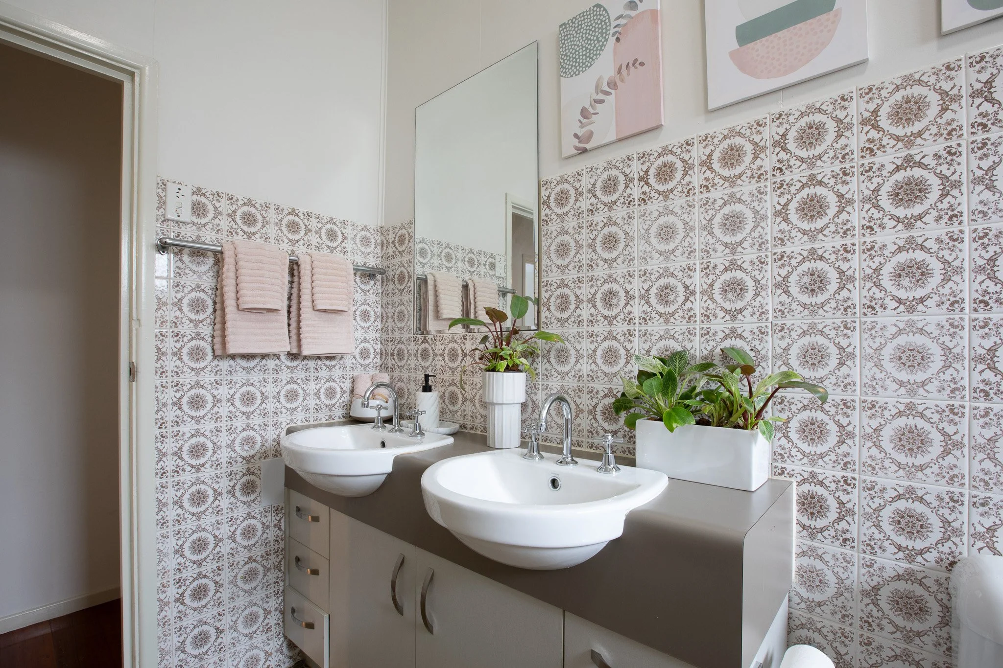 Bright, modern kitchen with white cabinetry, a black oven, a stovetop, a dishwasher, a double sink under a window, and an air conditioning unit on the wall. Hardwood flooring and a sliding glass door leading outside.