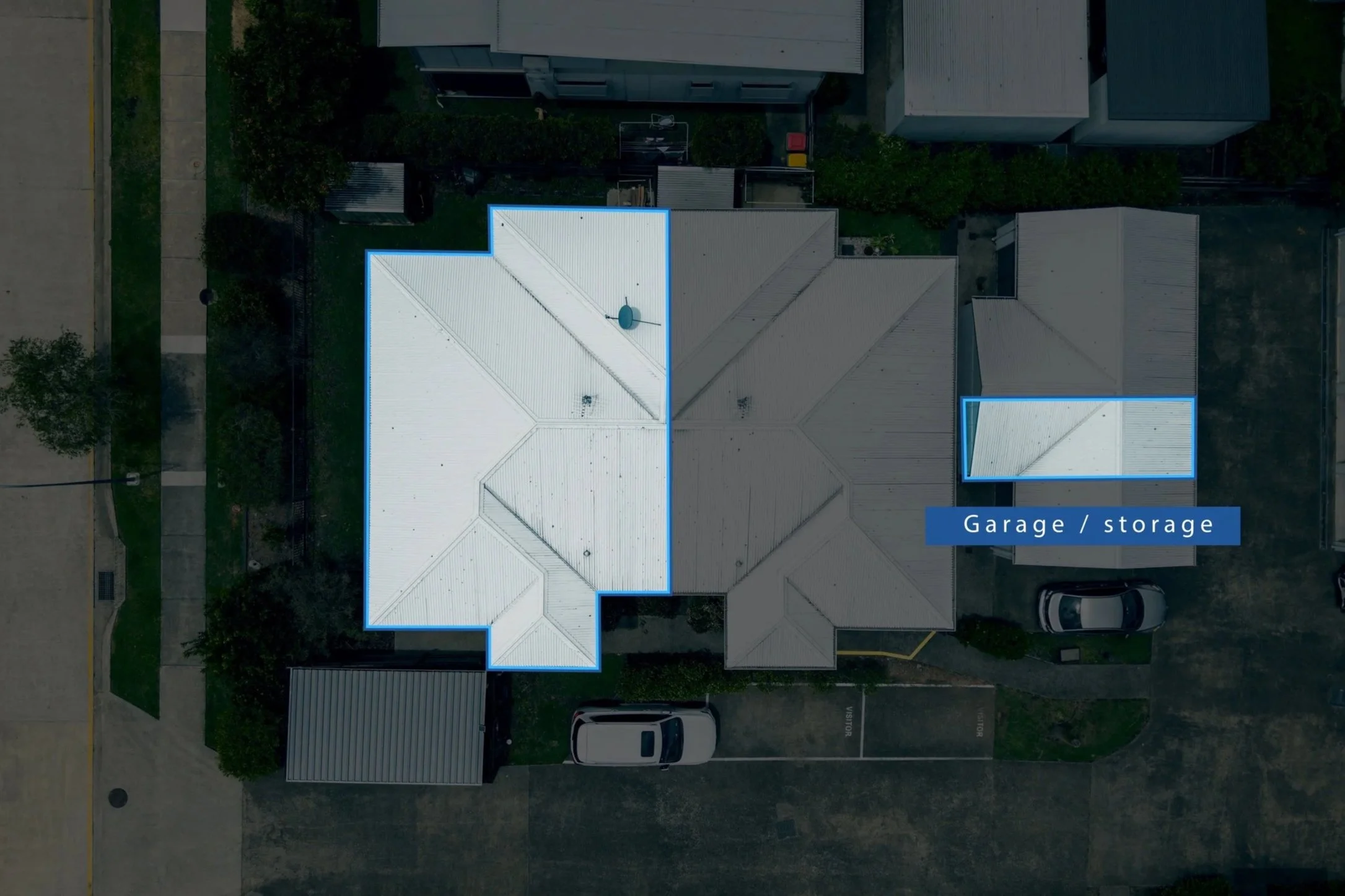 Aerial view of rooftops in a neighborhood, with sections outlined showing garage or storage areas and parking spaces for cars.