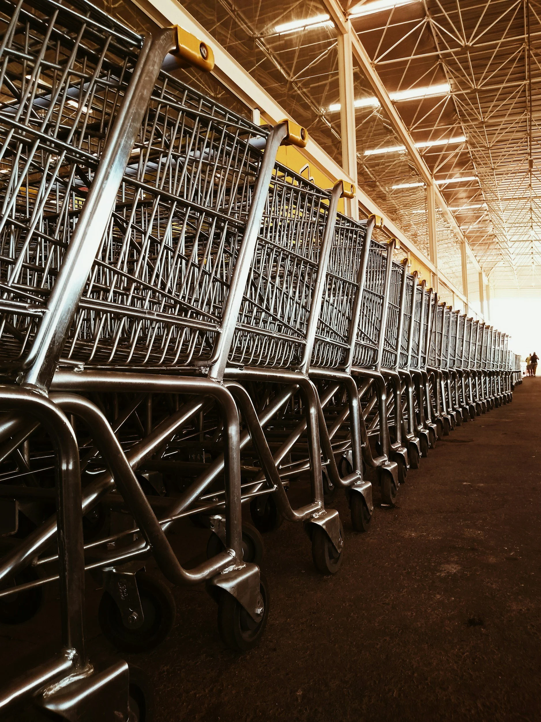 Multiple empty shopping carts lined up in a row outside a large retail store, with a high ceiling and bright lighting illuminating the parking lot area.