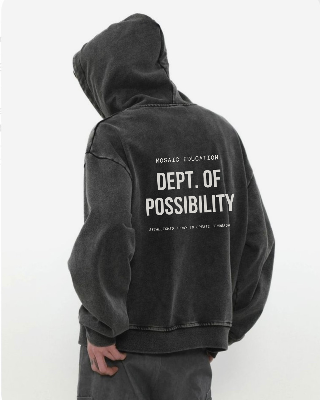Person wearing a dark hoodie with text that reads 'MOSAIC EDUCATION, DEPT. OF POSSIBILITY, ESTABLISHED TODAY TO CREATE TOMORROW,' standing against a plain white background.