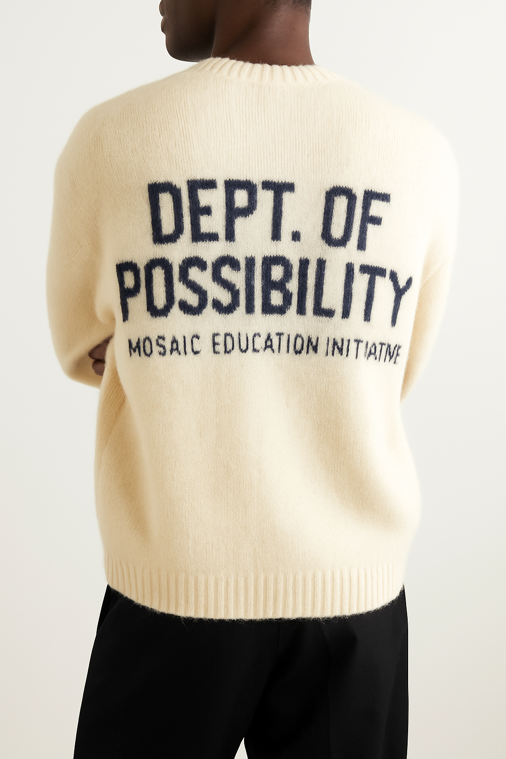Person wearing a cream-colored sweater with dark blue text that reads 'DEPT. OF POSSIBILITY MOSAIC EDUCATION INITIATIVE.'