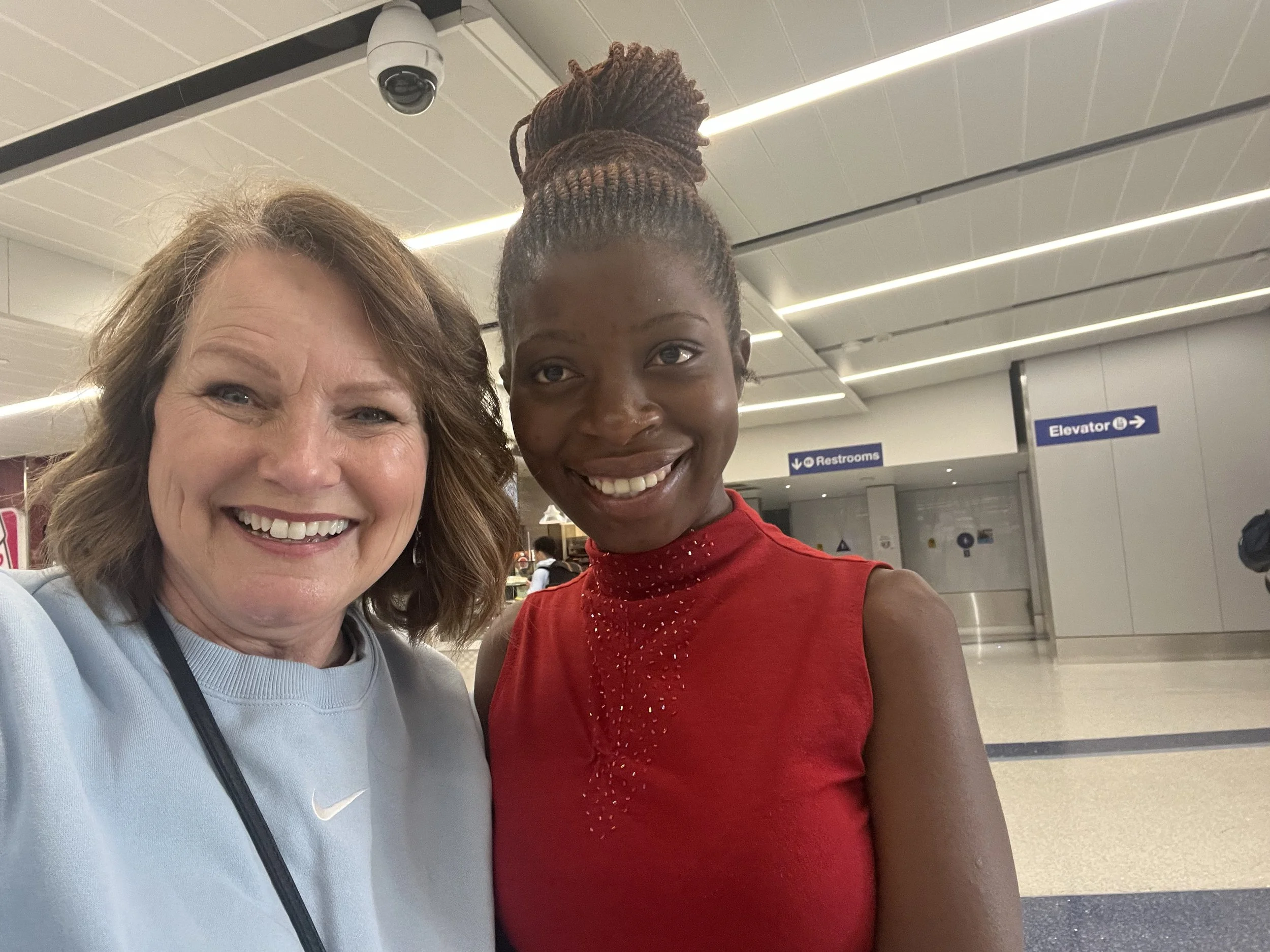 Two women smiling for a selfie in an airport terminal.