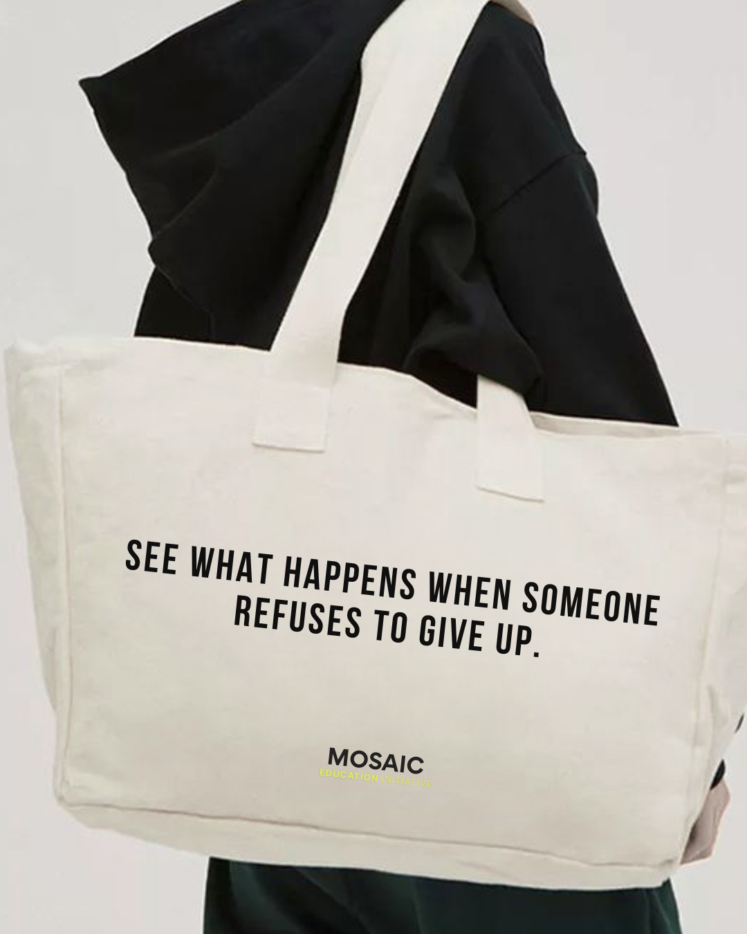 Person holding a large white tote bag with motivational text, wearing a black jacket.