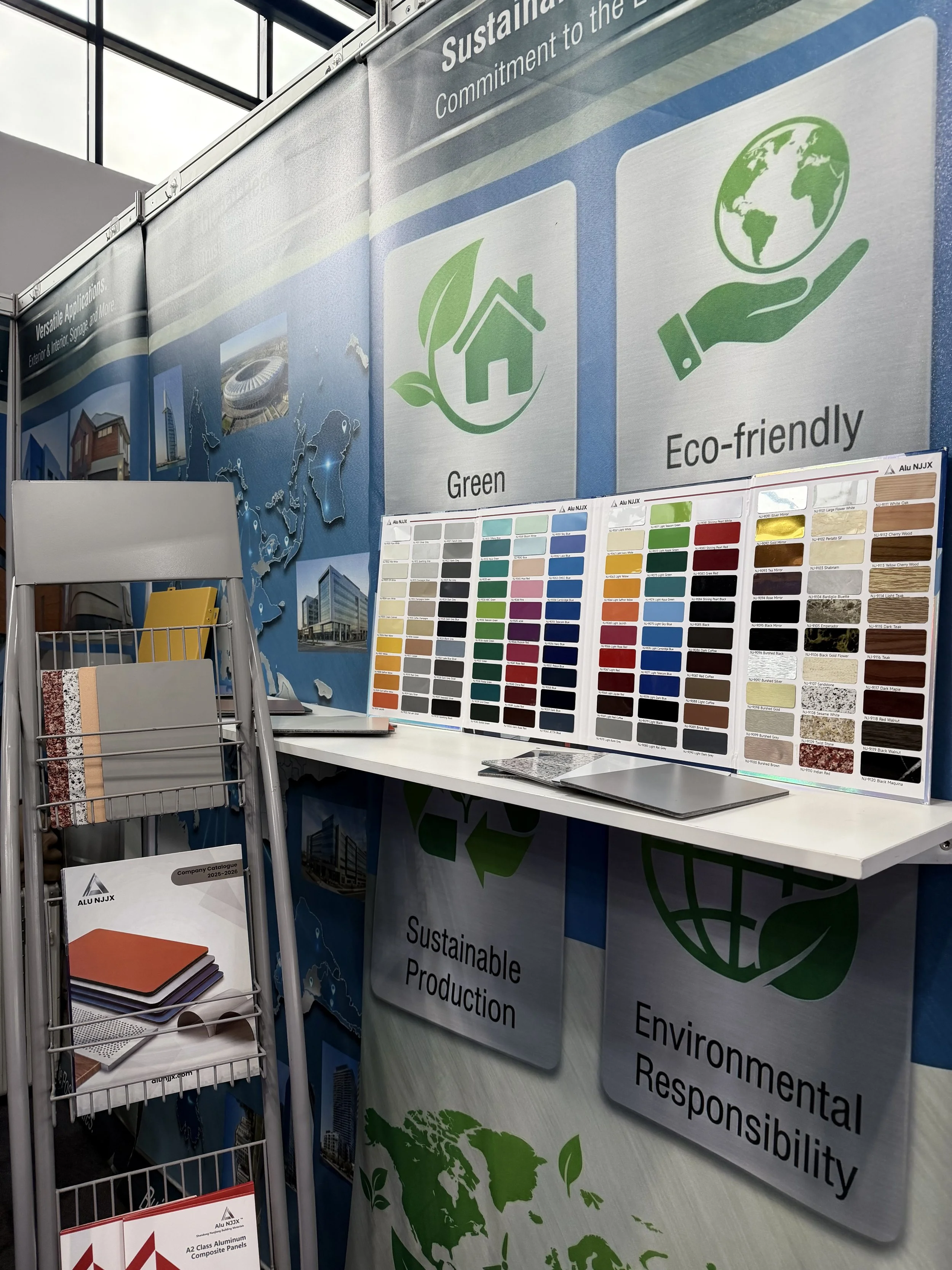 Booth display promoting sustainable and eco-friendly products with signs showing a green house icon, a hand holding the earth, and text about sustainability, environmental responsibility, and green production. Included are color sample charts and bro