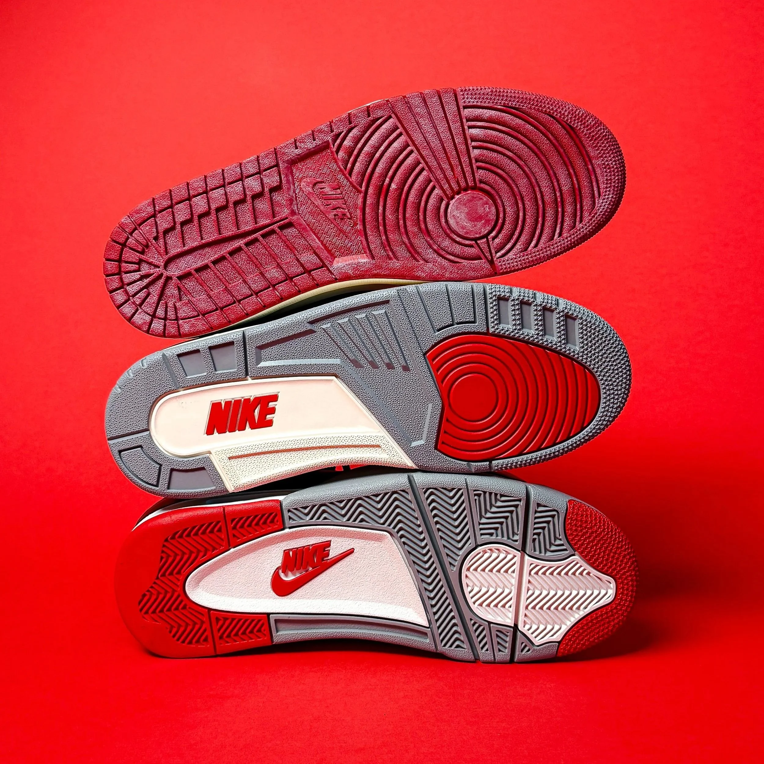 Stacked Nike shoe soles showing red, gray, and white traction patterns against a red background