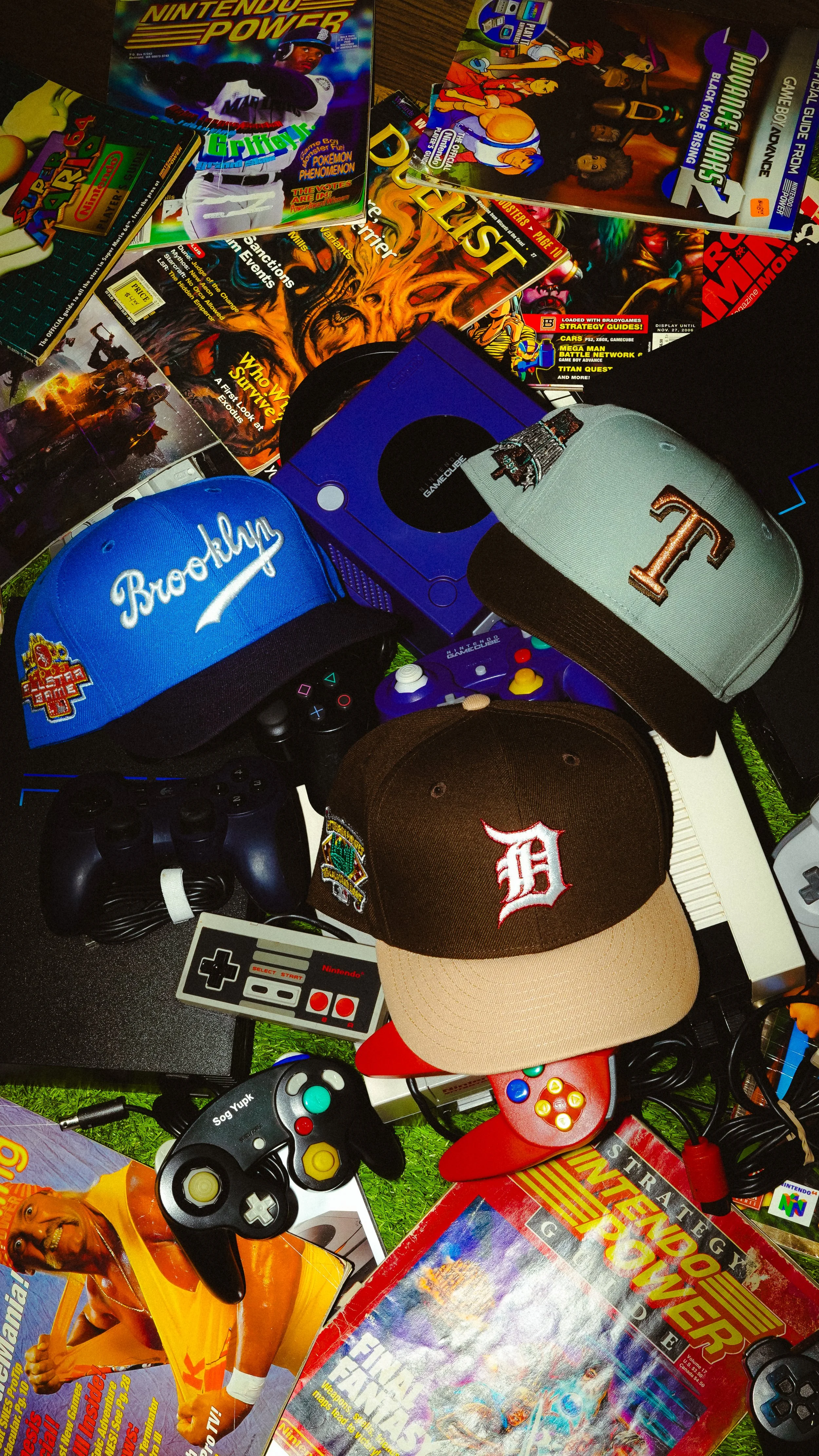 Collection of vintage video game magazines, Nintendo and PlayStation controllers, GameCube accessories, retro gaming hats, and electronics arranged on a floor