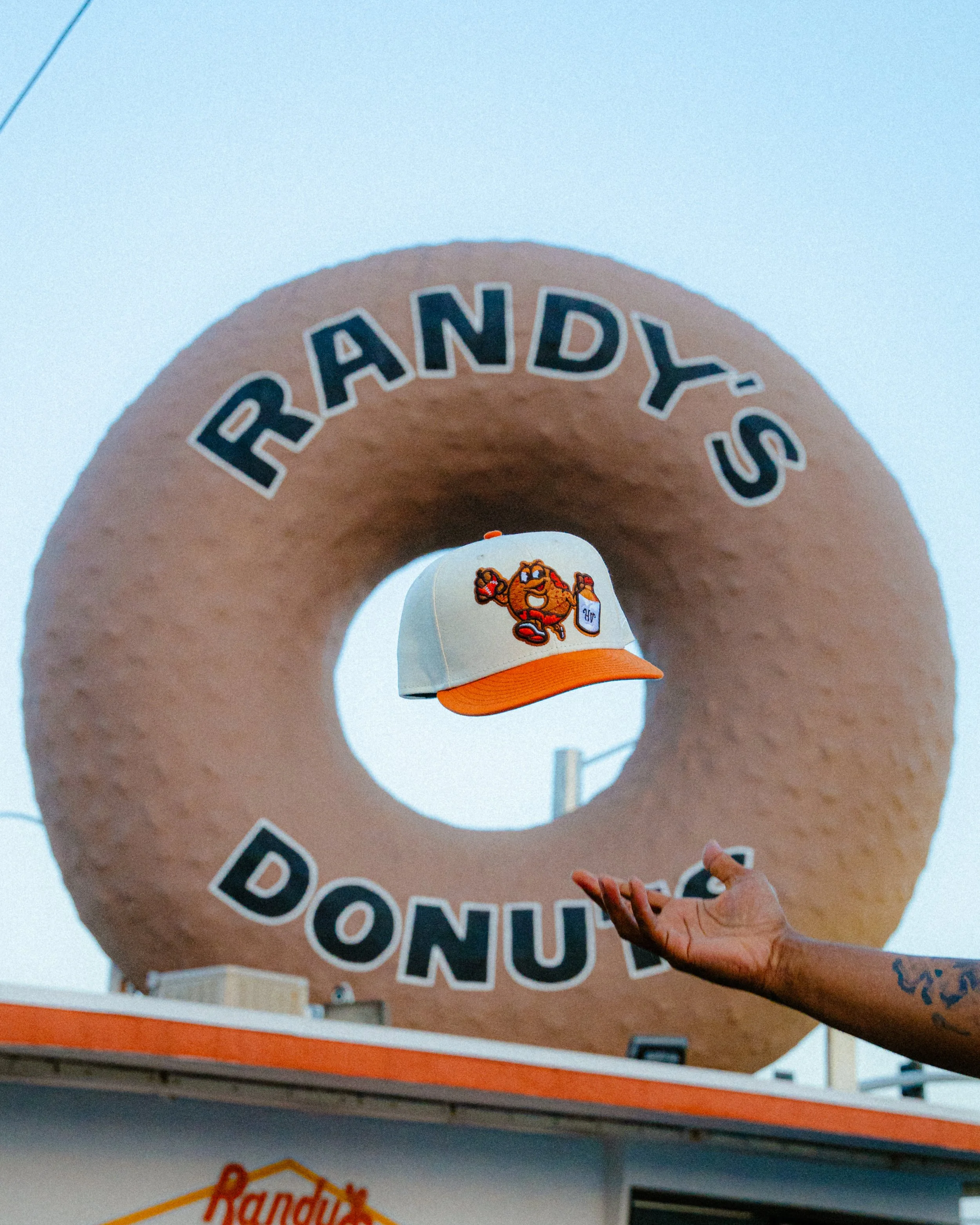 Close-up of a person wearing a white and orange cap featuring a cartoon football player, in front of a large mascot graphic and partial sports lettering.