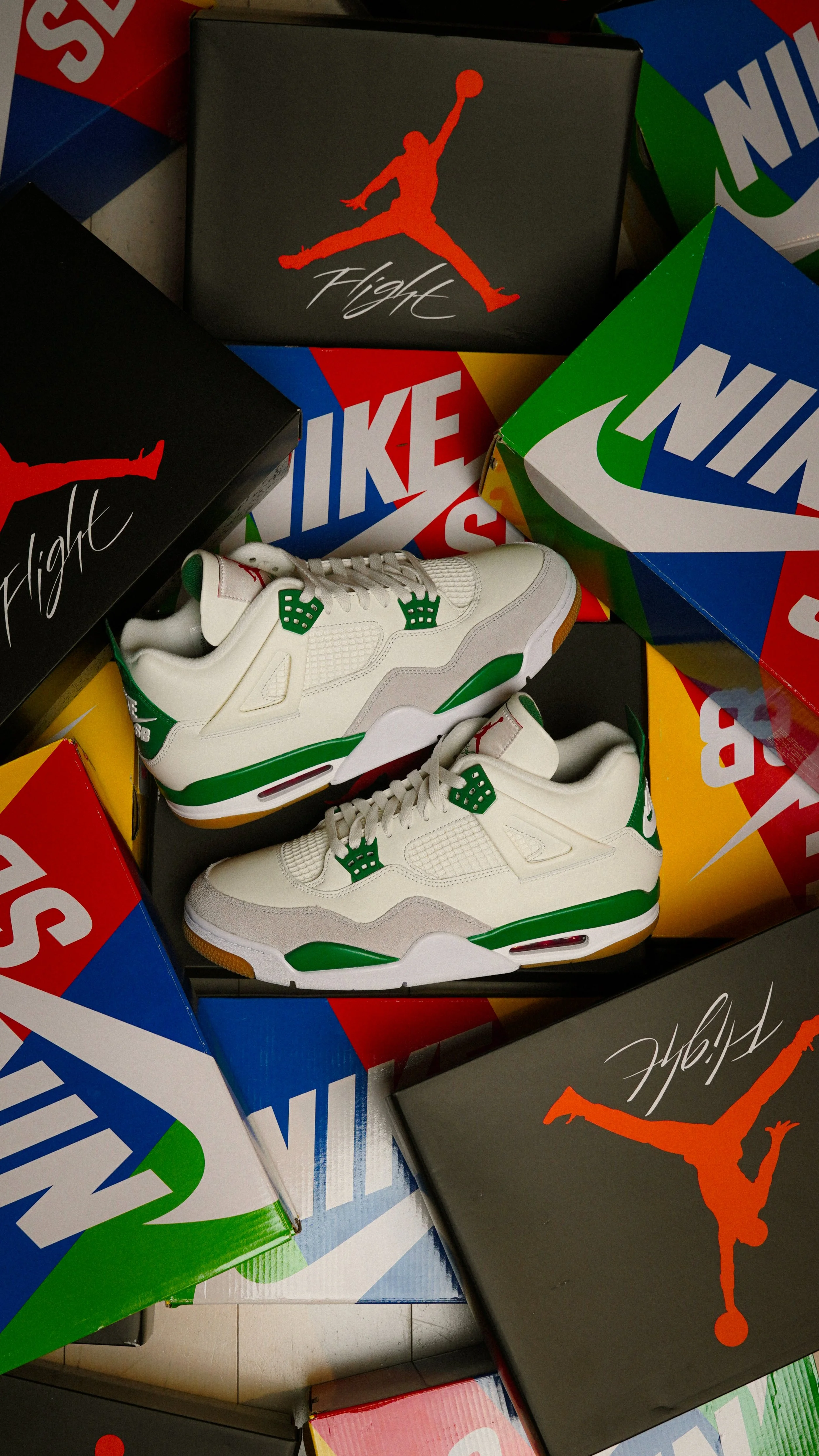 White and green basketball sneakers displayed on black Jordan shoeboxes, surrounded by colorful Nike shoeboxes.