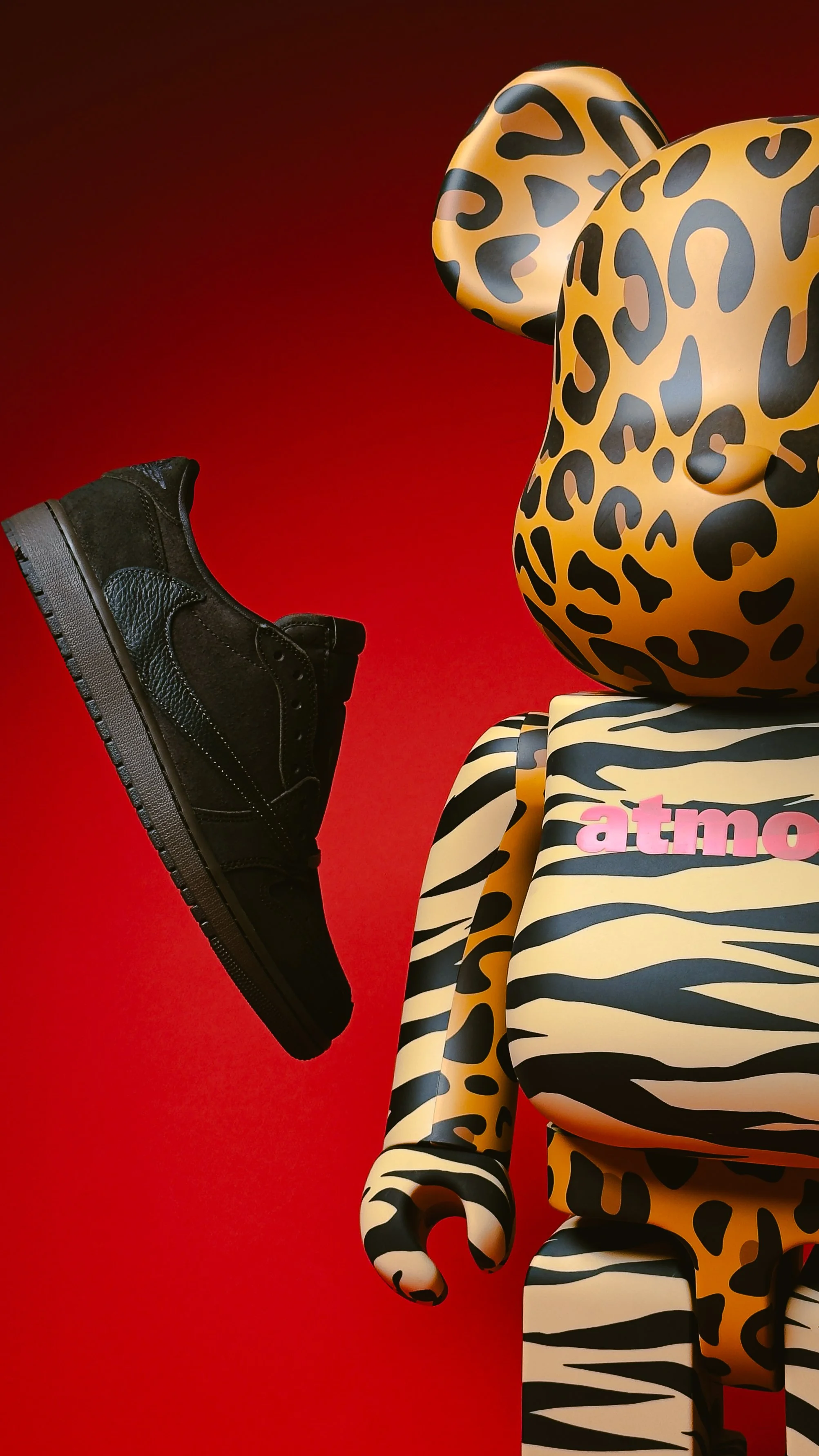 Stylized mannequin in leopard-print and zebra-striped clothing beside a black sneaker against a red background