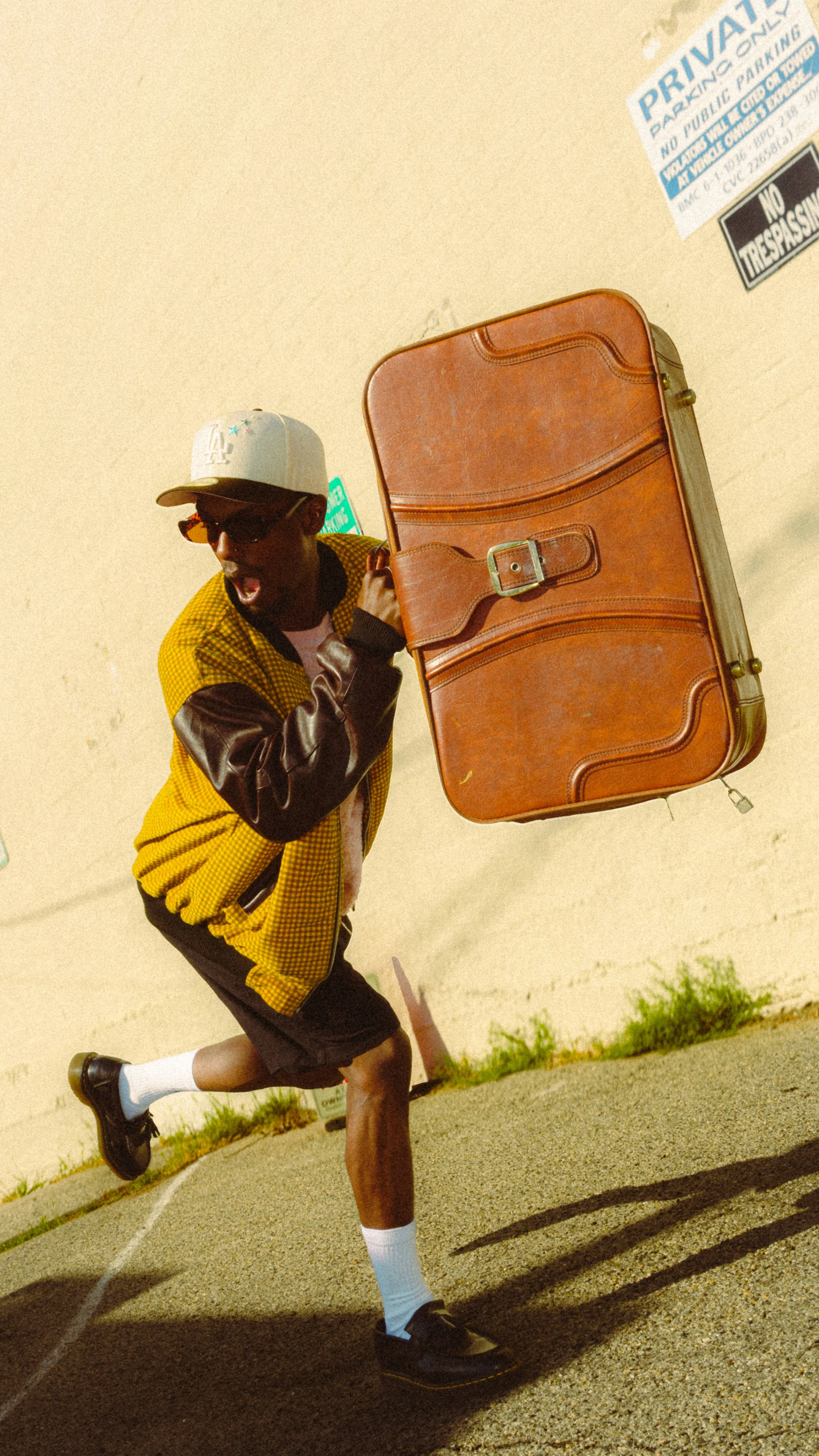 Stylized close-up of a runner in yellow checkered clothing, black gloves, white socks, and black shoes beside a vintage brown leather suitcase on a track.