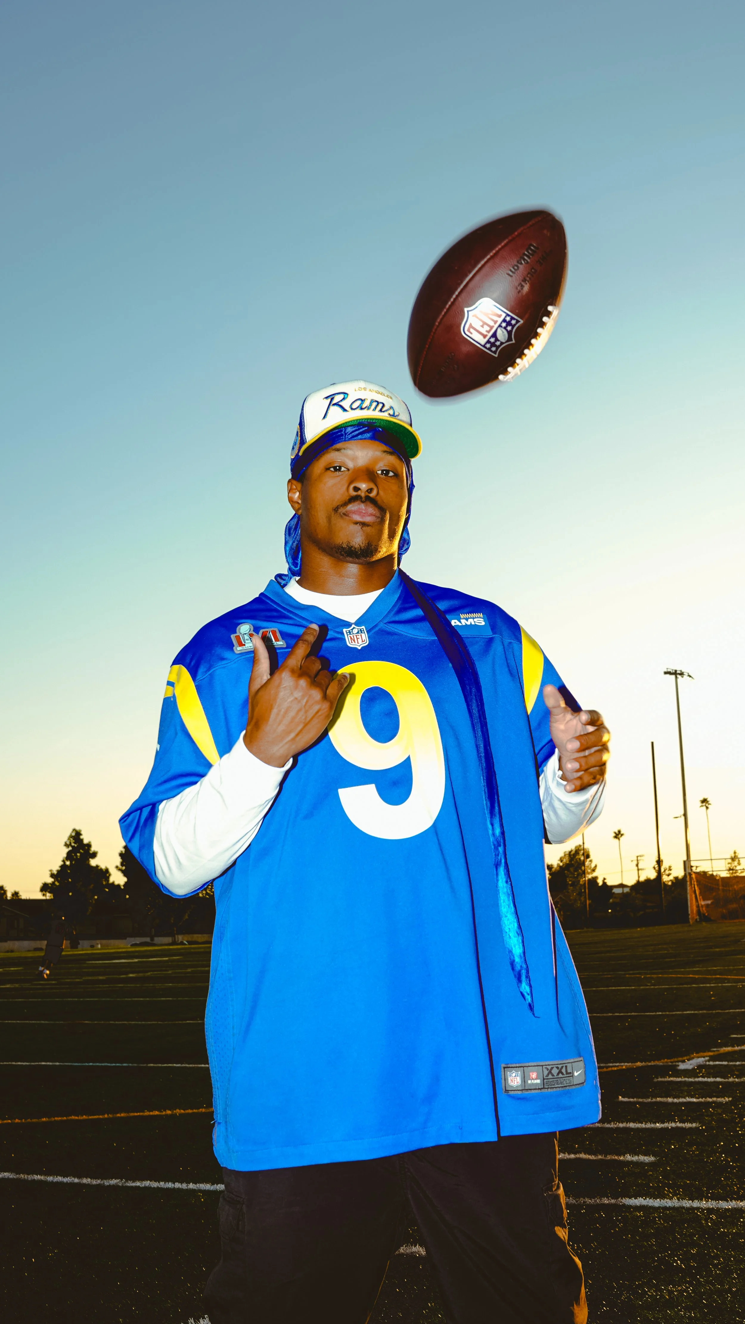 Man wearing a Los Angeles Rams football jersey and cap on a field with an NFL football floating above him