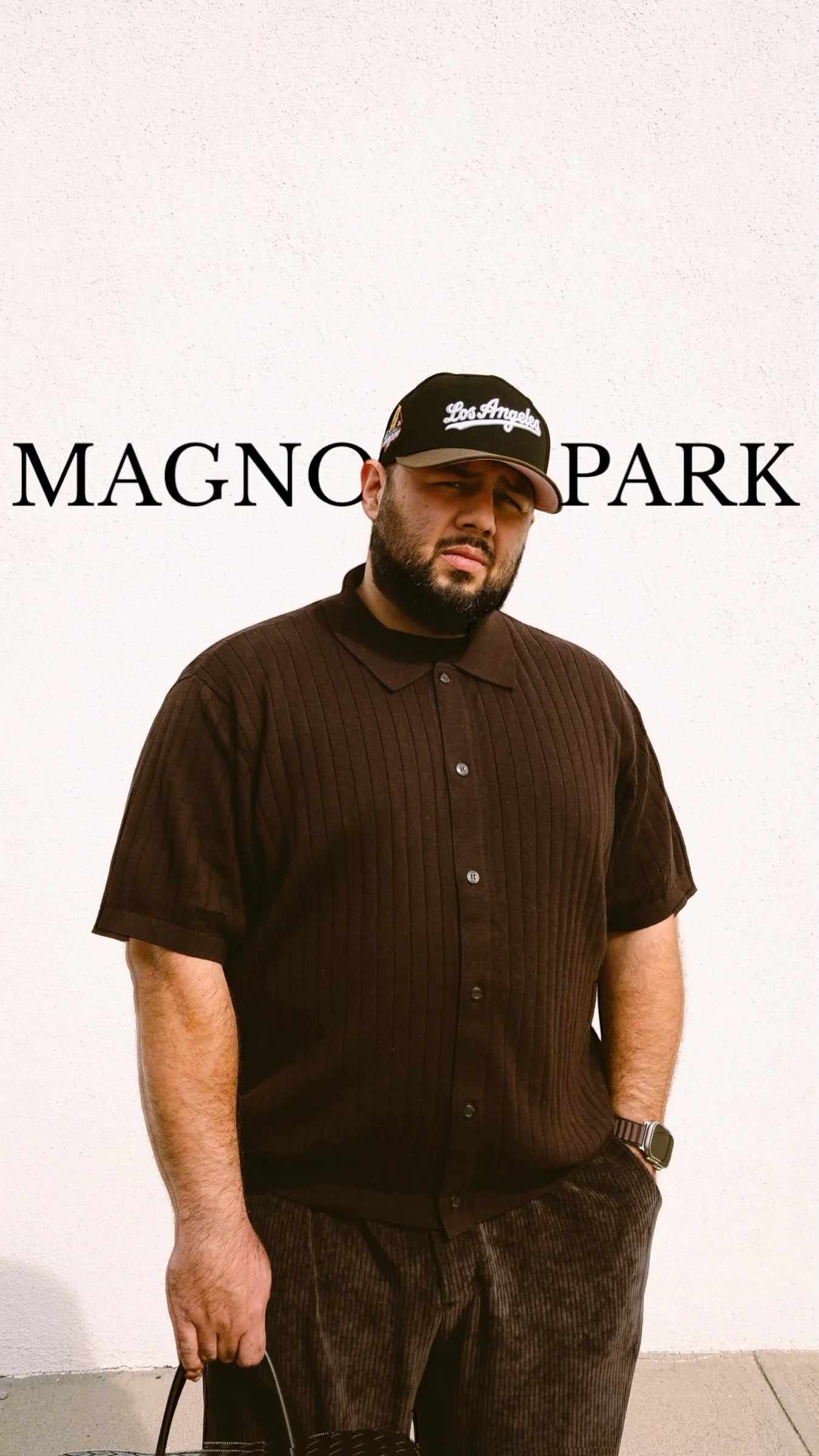 Bearded man wearing a Los Angeles baseball cap and brown outfit in front of a MAGNO PARK backdrop
