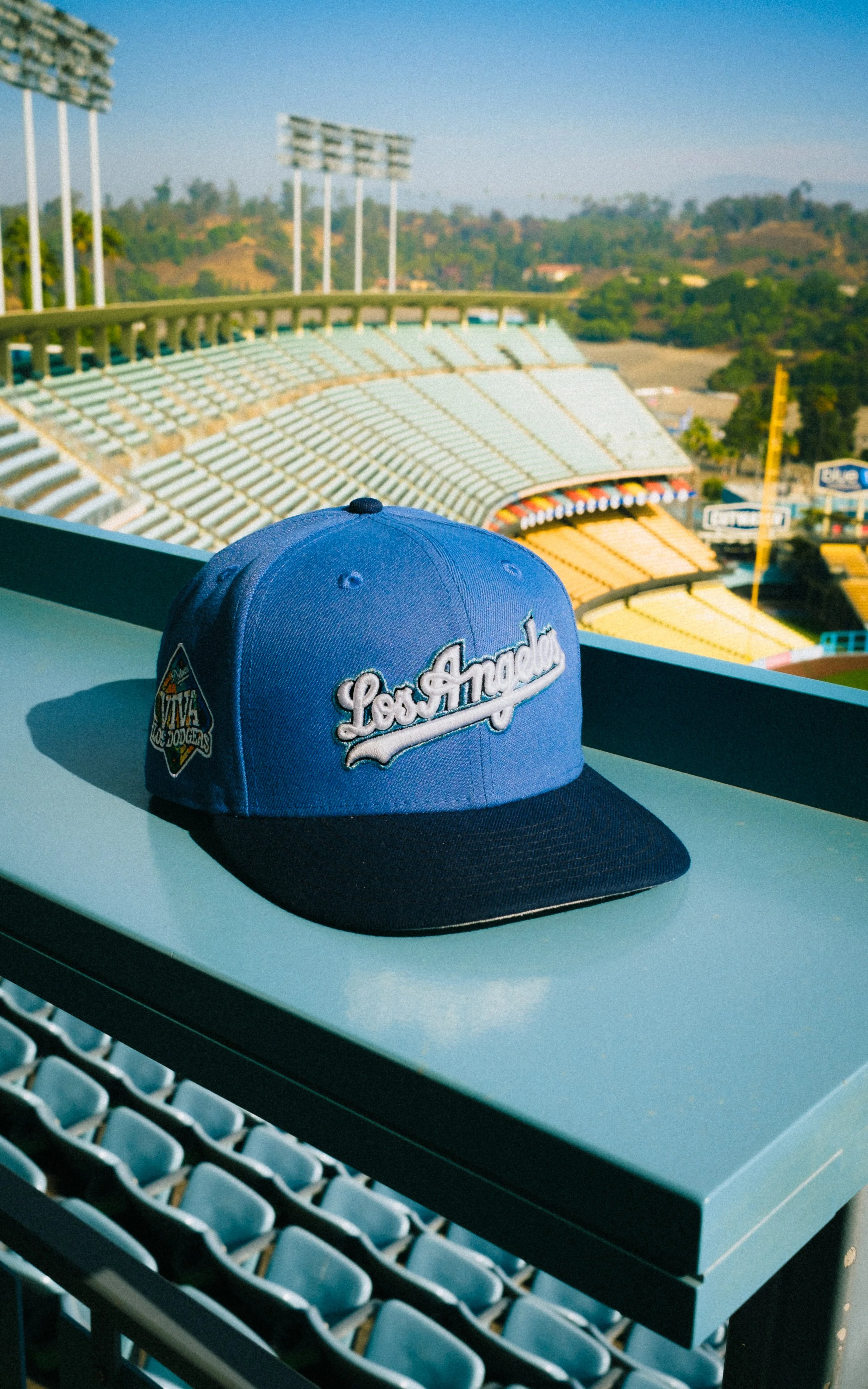 Blue Los Angeles baseball cap resting on stadium seats overlooking an empty baseball field