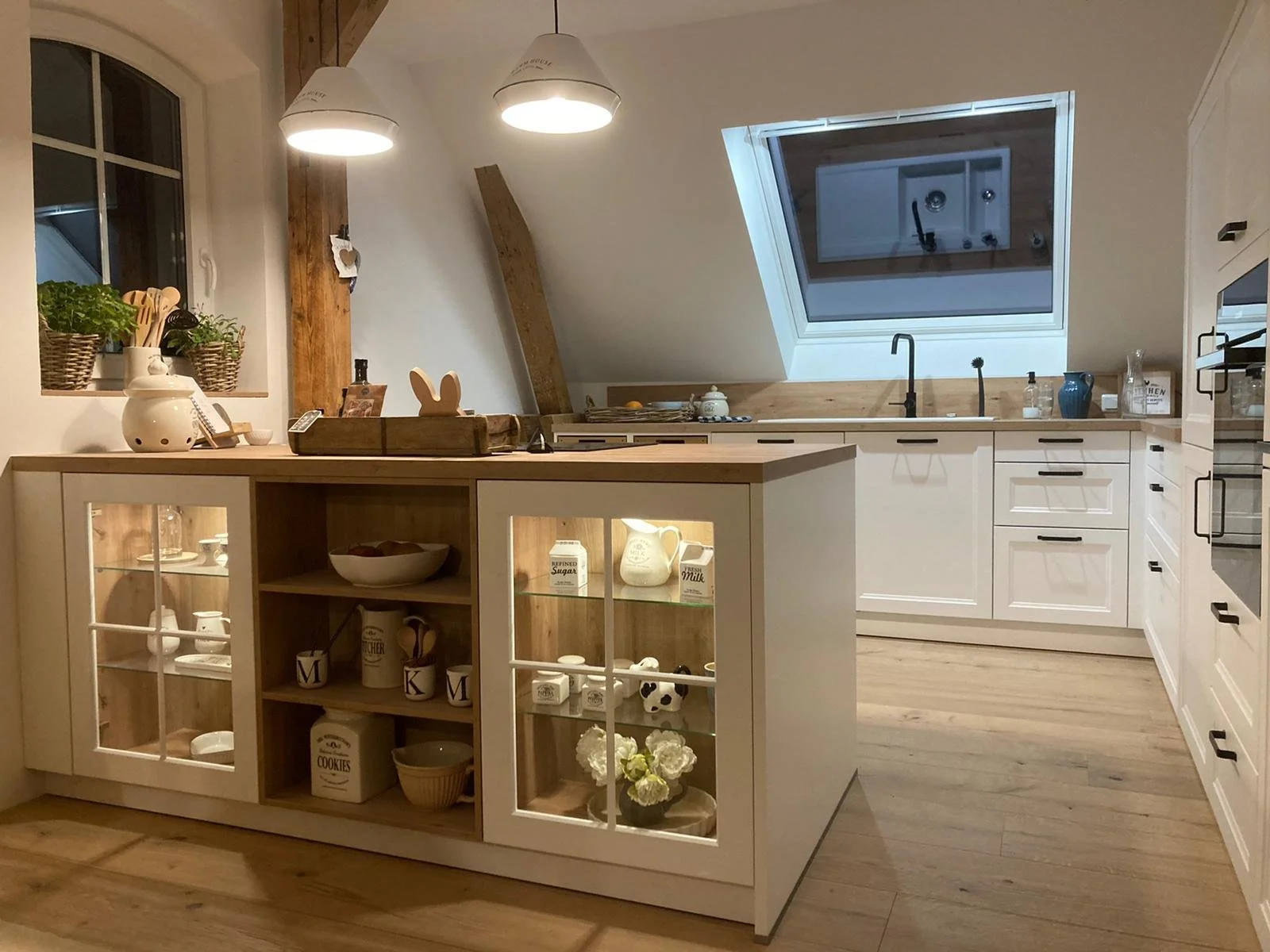 Moderne Küche mit weißen Schränken und Holzelementen, ein Fenster und eine Dachfenster, offene Regale, Küchenutensilien auf der Insel, Dekorationsgegenstände und Küchengeräte