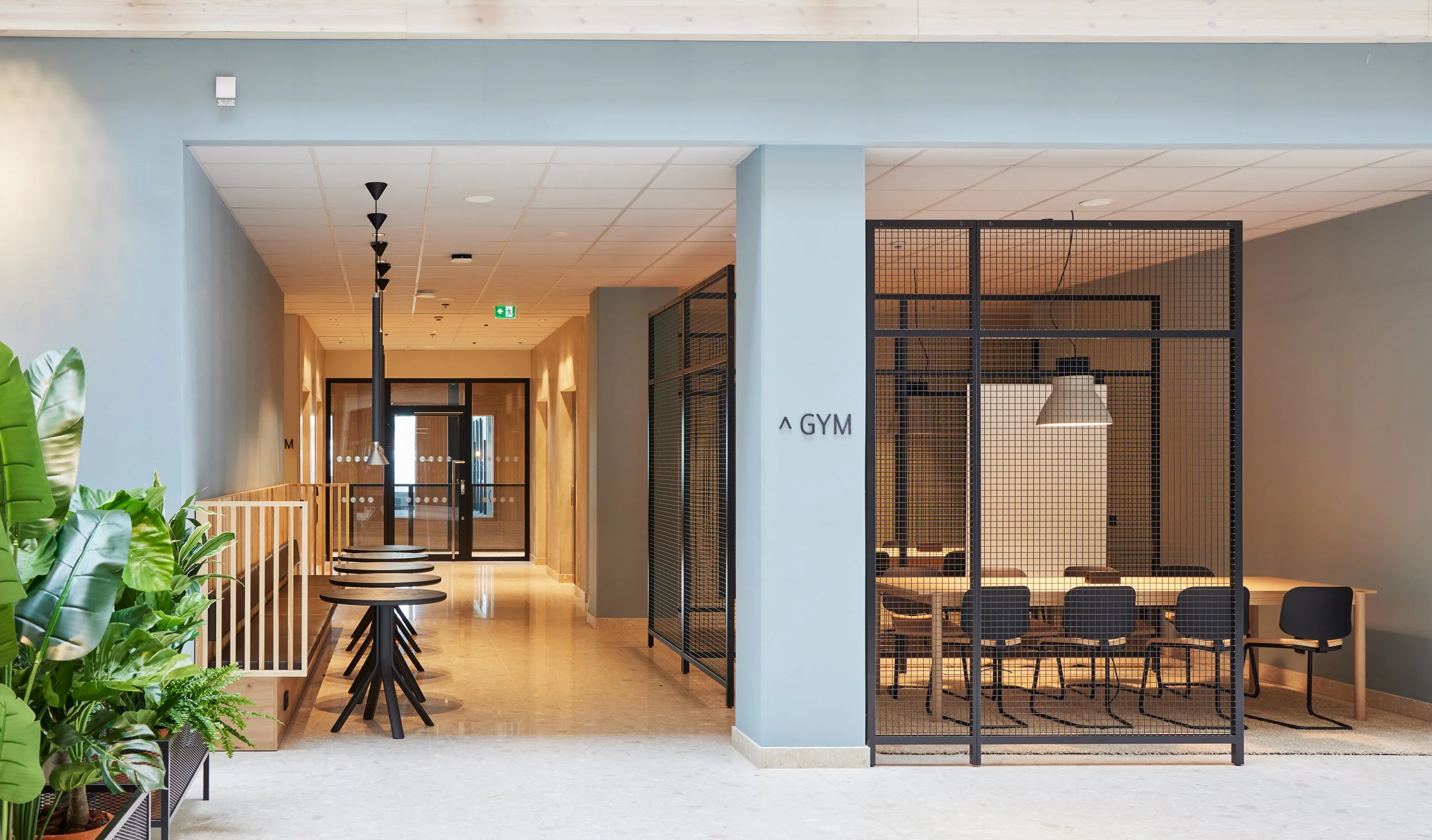 Interiör av ett modernt gym med träningsrum och matsal, utgång till en korridor.