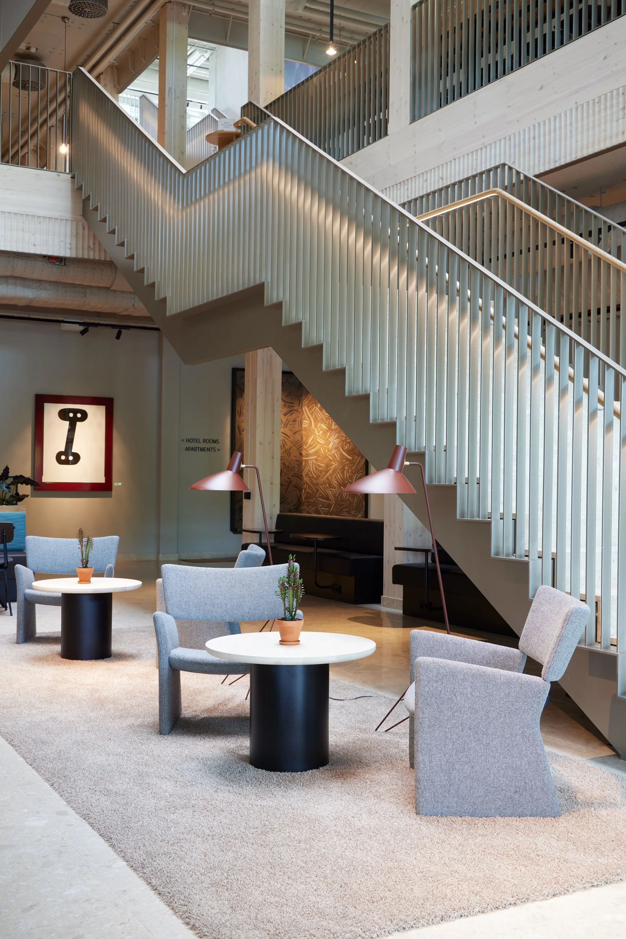 Trivsamt hotellobby med sittplatser, små bord med kaktusar, läslampor och en modern trapphall i trä och metall.