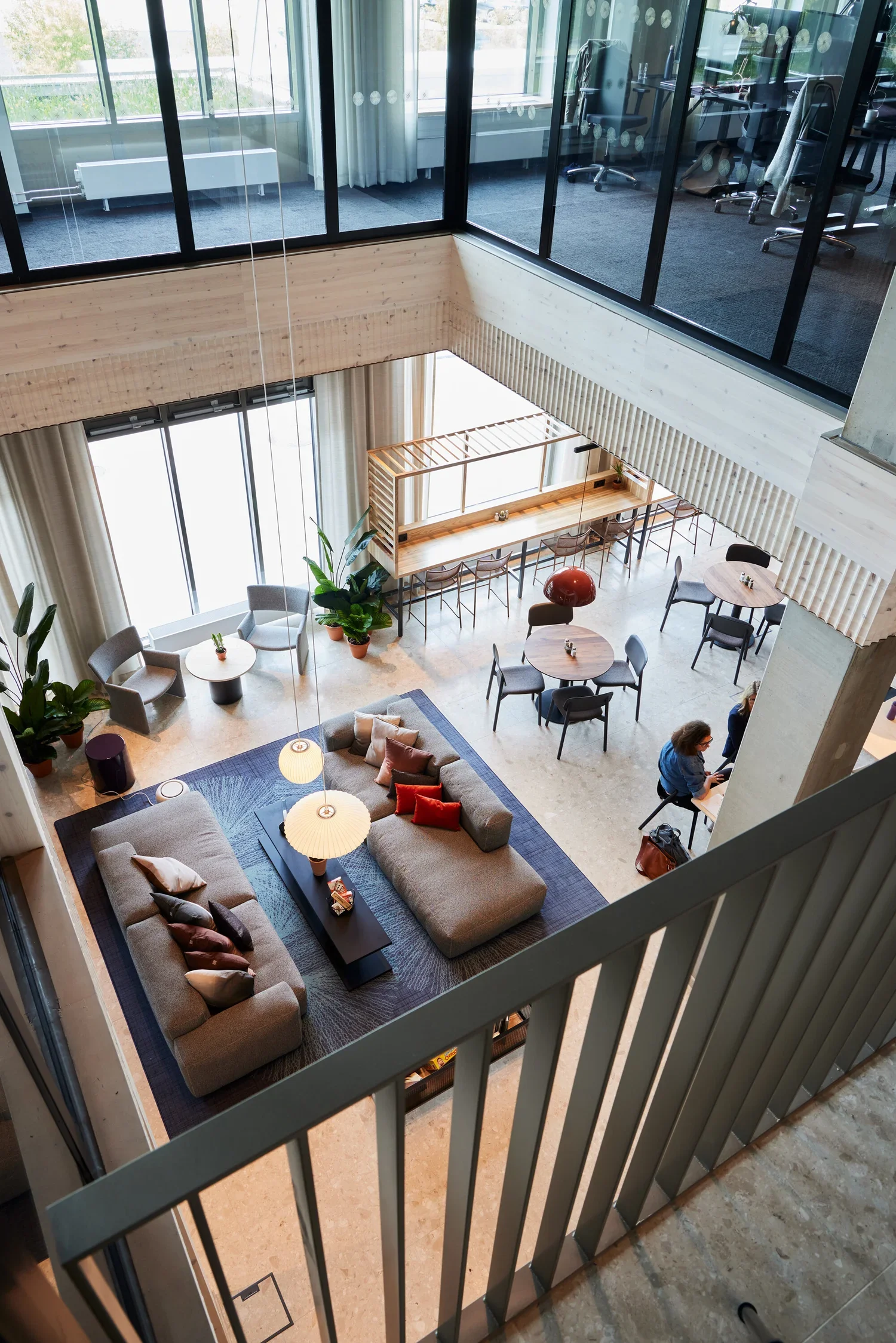 Inomhusbild av ett modernt kontorshotell med soffgrupp, växter, matbord och arbetsplatser på andra våningen.