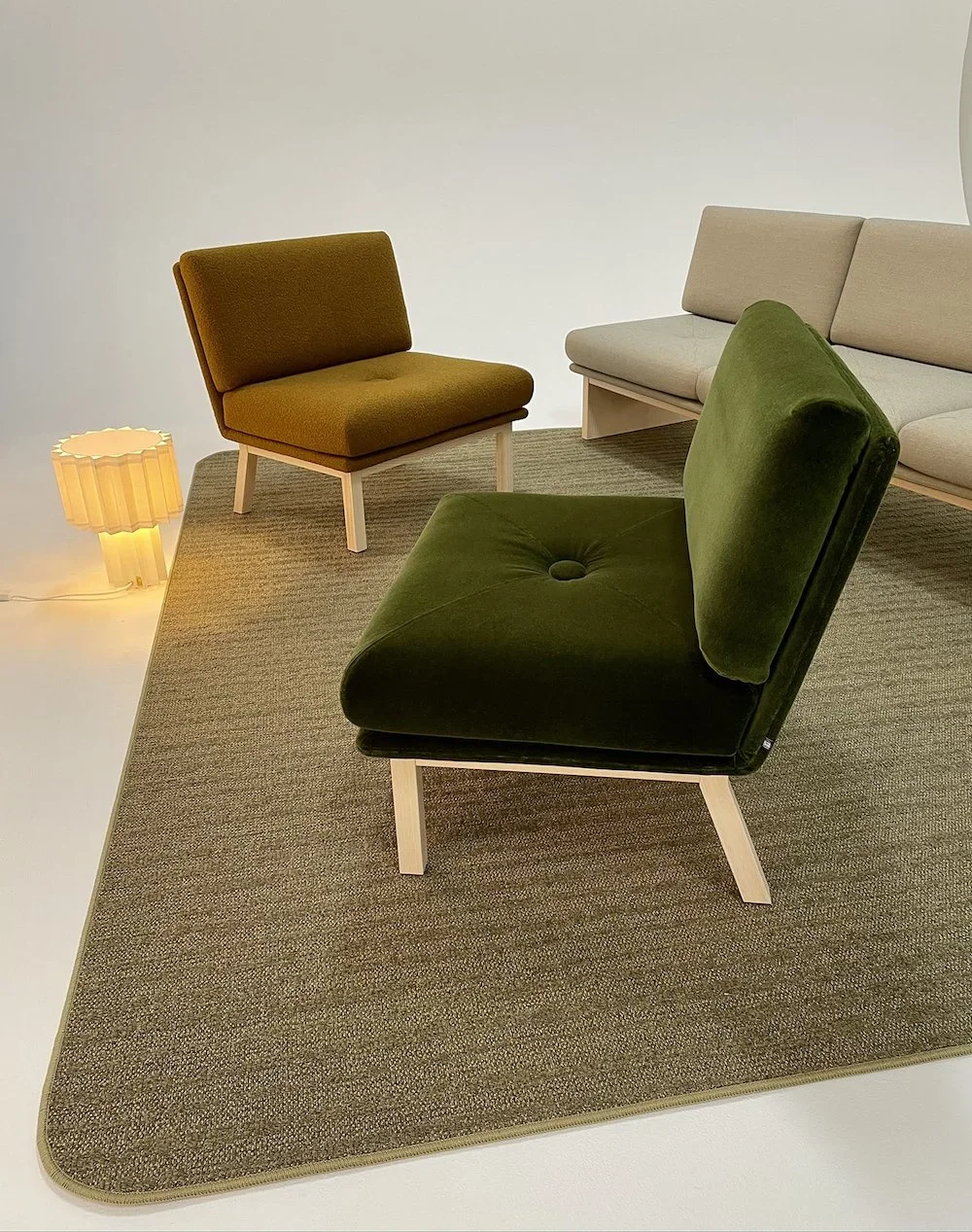 Väggdekorerat vardagsrum med gröna och beige sittmöbler på en beige matta, med en gul belysning på vänster sida.