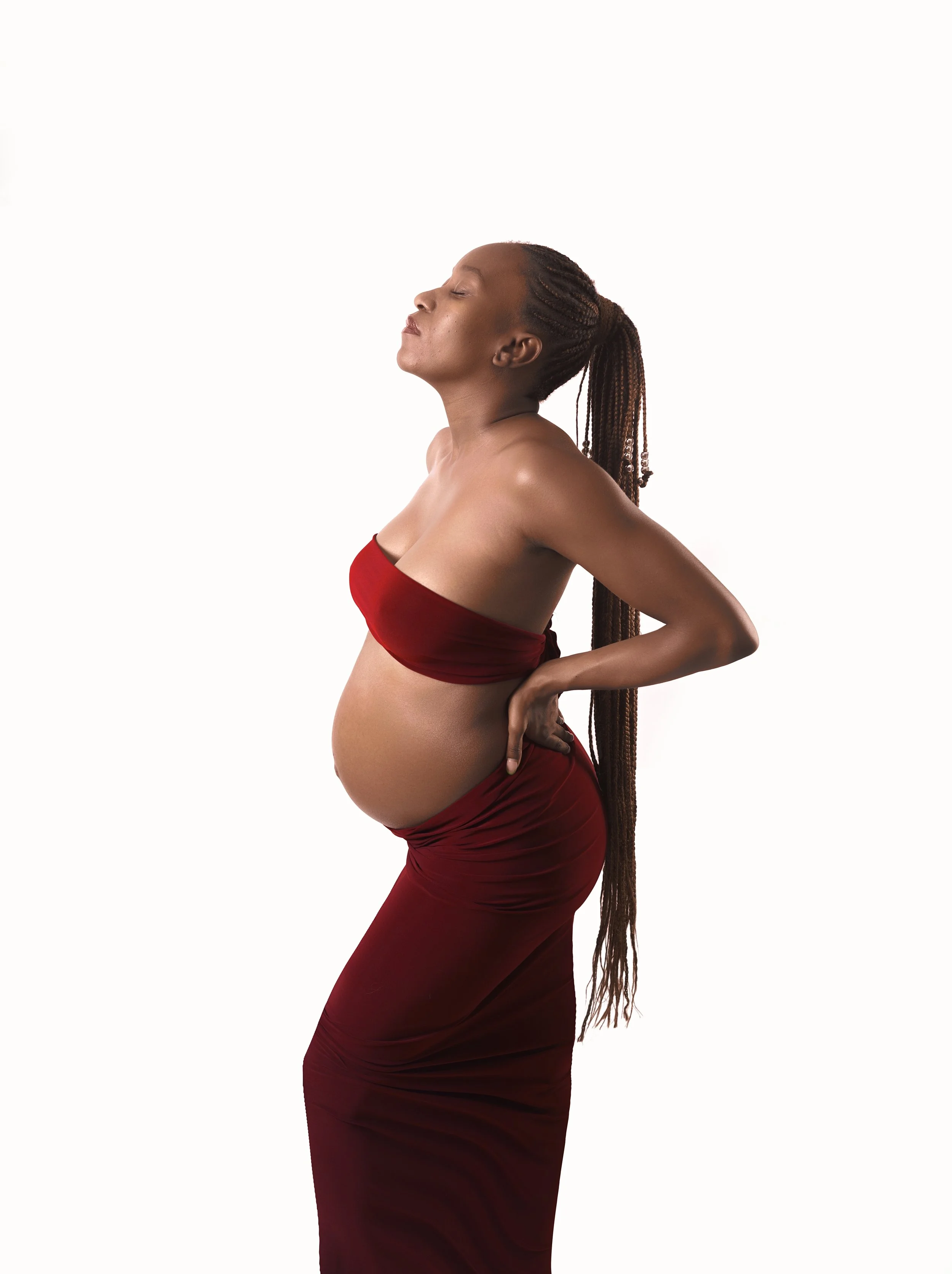 Femme enceinte, portant un haut rouge et une jupe longue rouge, avec les yeux fermés, en pose de relaxation, contre un fond blanc.