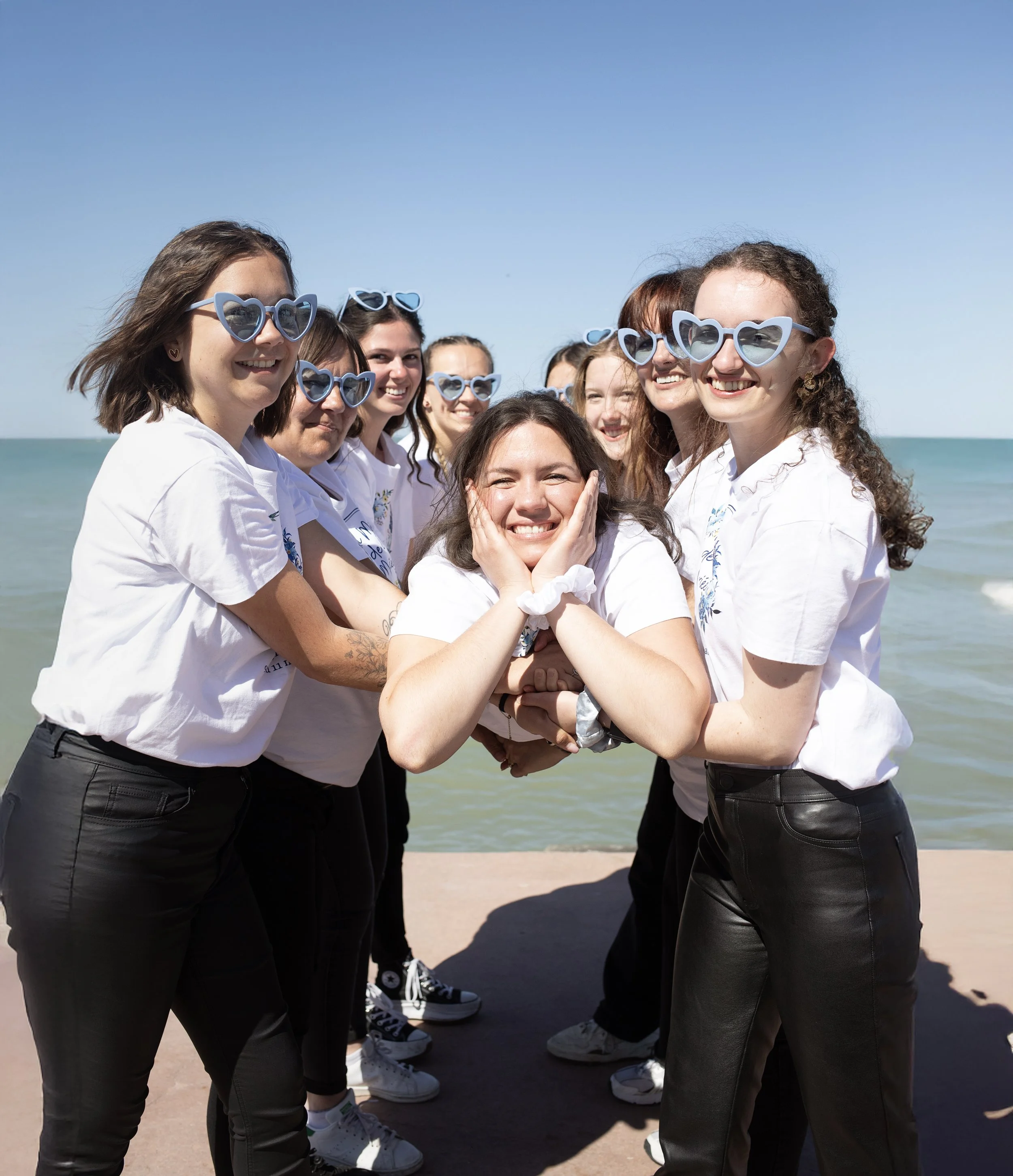 Groupe de jeunes femmes souriantes portant des lunettes de soleil bleues en forme de cœurs sur la plage.