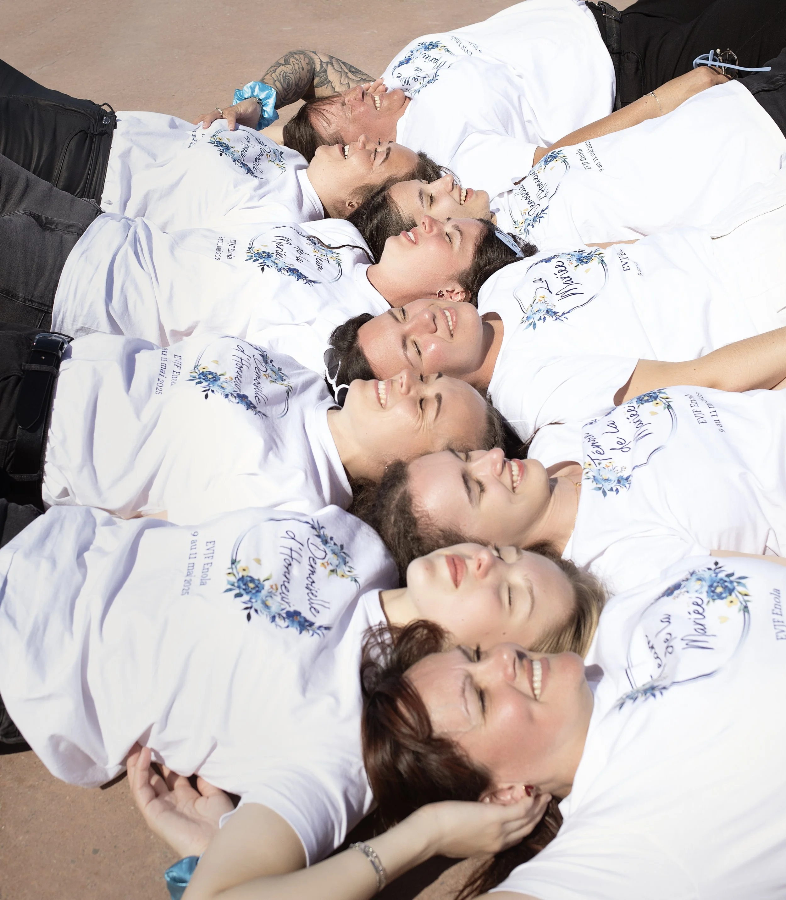Groupe de personnes allongées sur le sol, portant des T-shirts blancs avec un diagramme floral en bleu et le texte en français.