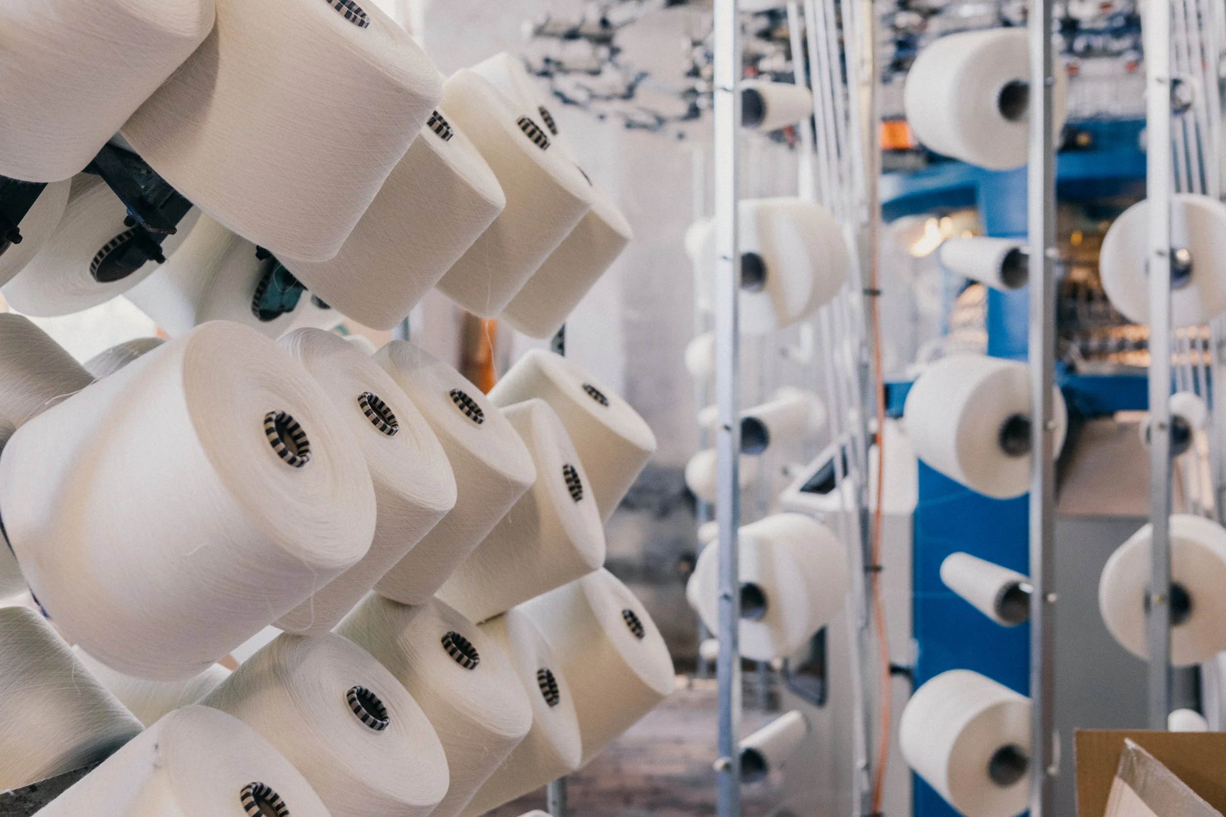 Rows of large white spools of thread stored on metal racks in a textile factory