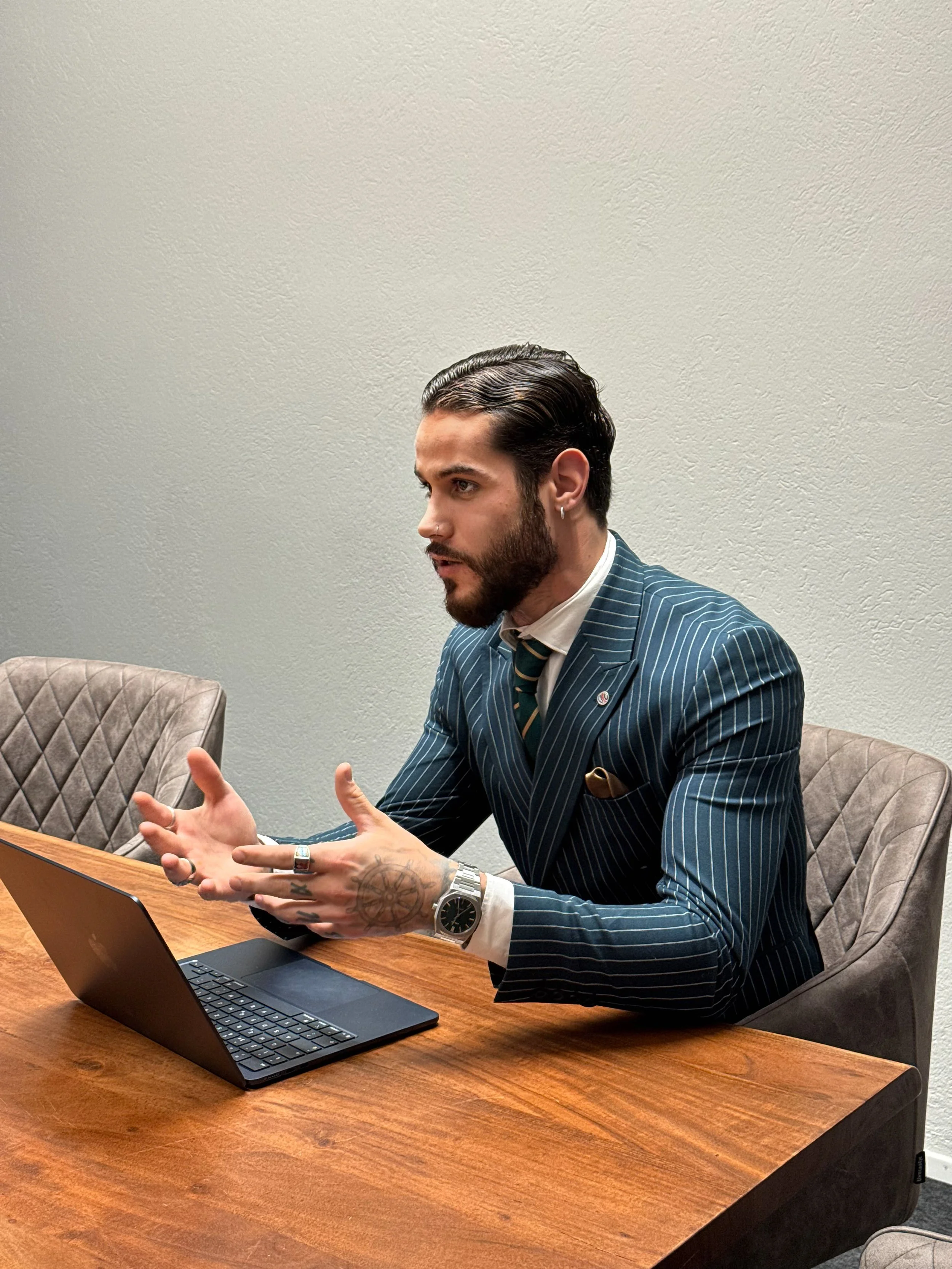 Mann im Anzug sitzt an einem Tisch mit einem Laptop und spricht.