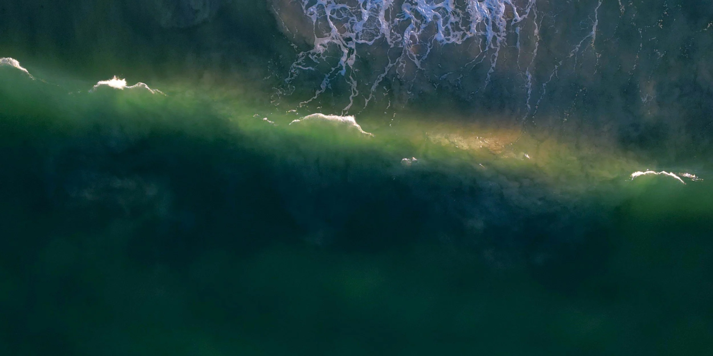 Aerial view of ocean waves with a greenish hue and some foam at the crests