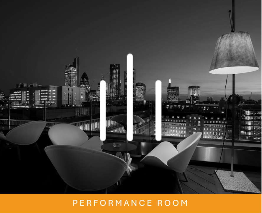 A modern performance room with a city skyline view at night, featuring a seating area with chairs, a small table, large vertical light bars, and a hanging lamp.