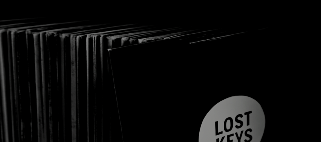 A stack of vinyl records, with one record sleeve labeled "Lost Keys" in the foreground, in a dimly lit setting.