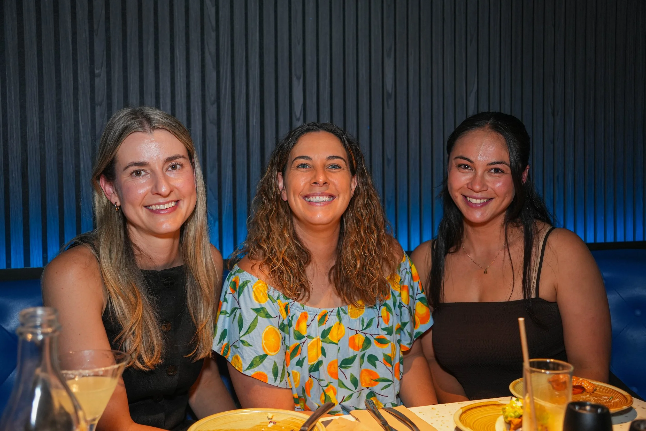 Three women sitting together at a table in a restaurant, smiling at the camera.