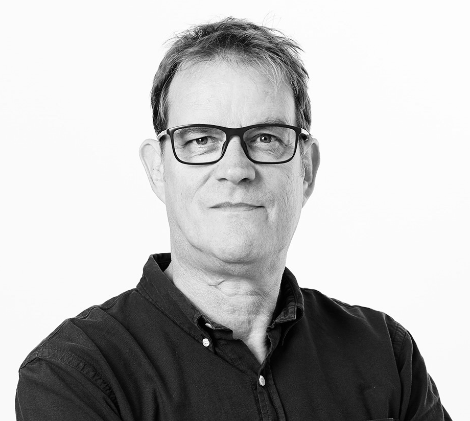 Black and white portrait of a middle-aged man with glasses, short hair, and a slight smile, wearing a black button-up shirt.