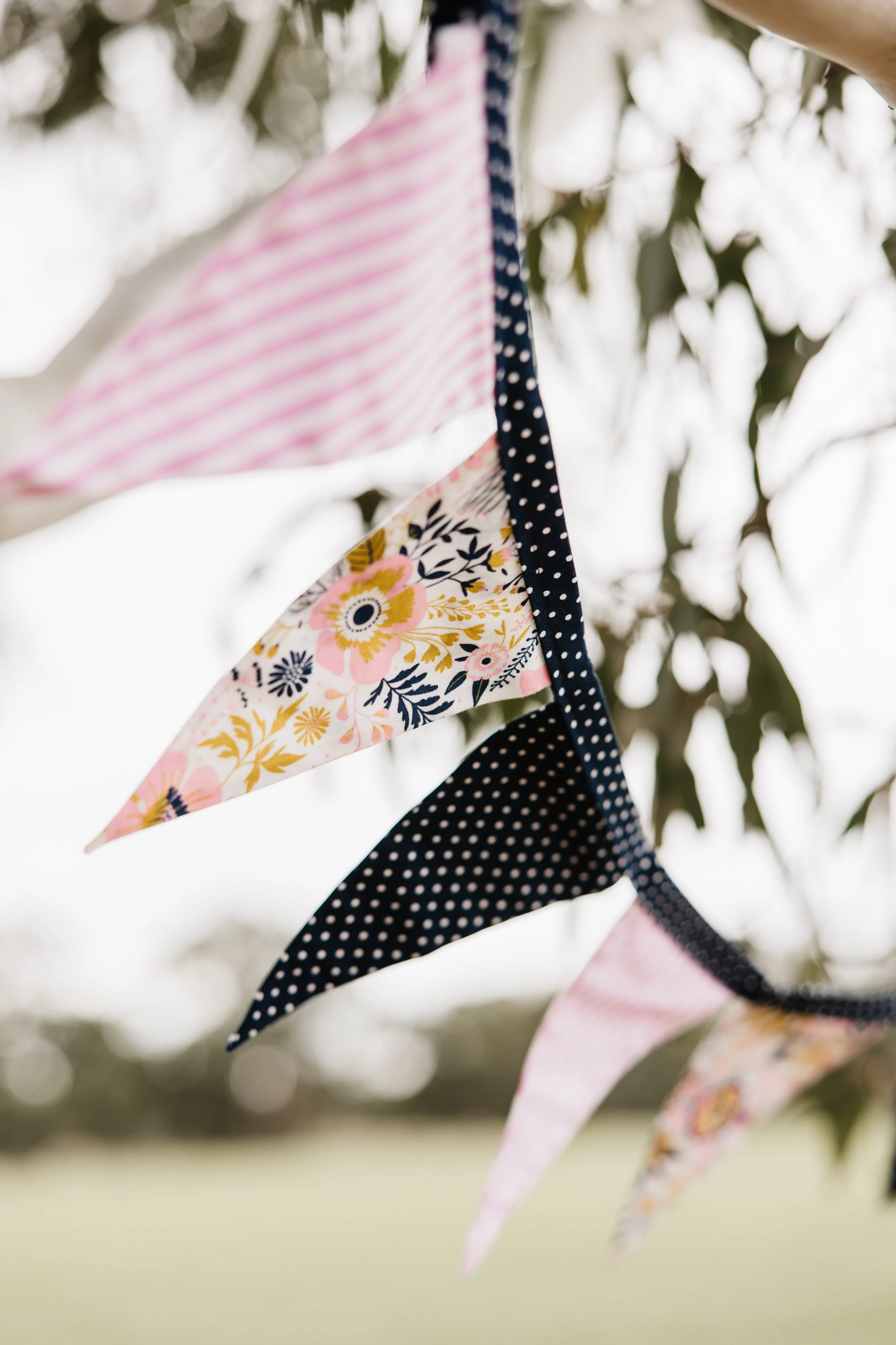 Colorful fabric bunting with floral, polka dot, and striped patterns hanging outdoors.