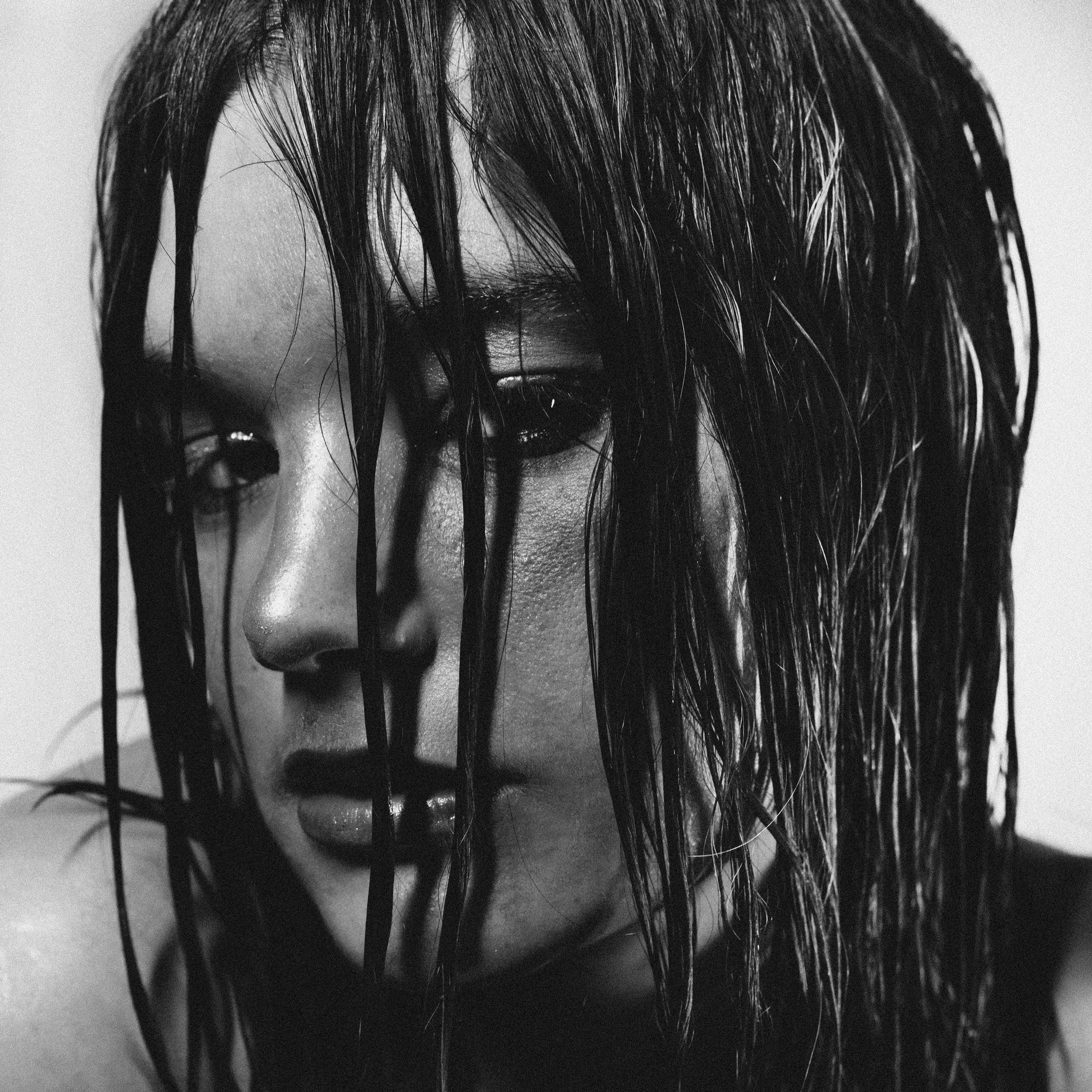 Portrait en noir et blanc d'une femme avec des cheveux mouillés couvrant partiellement son visage, expression mélancolique.