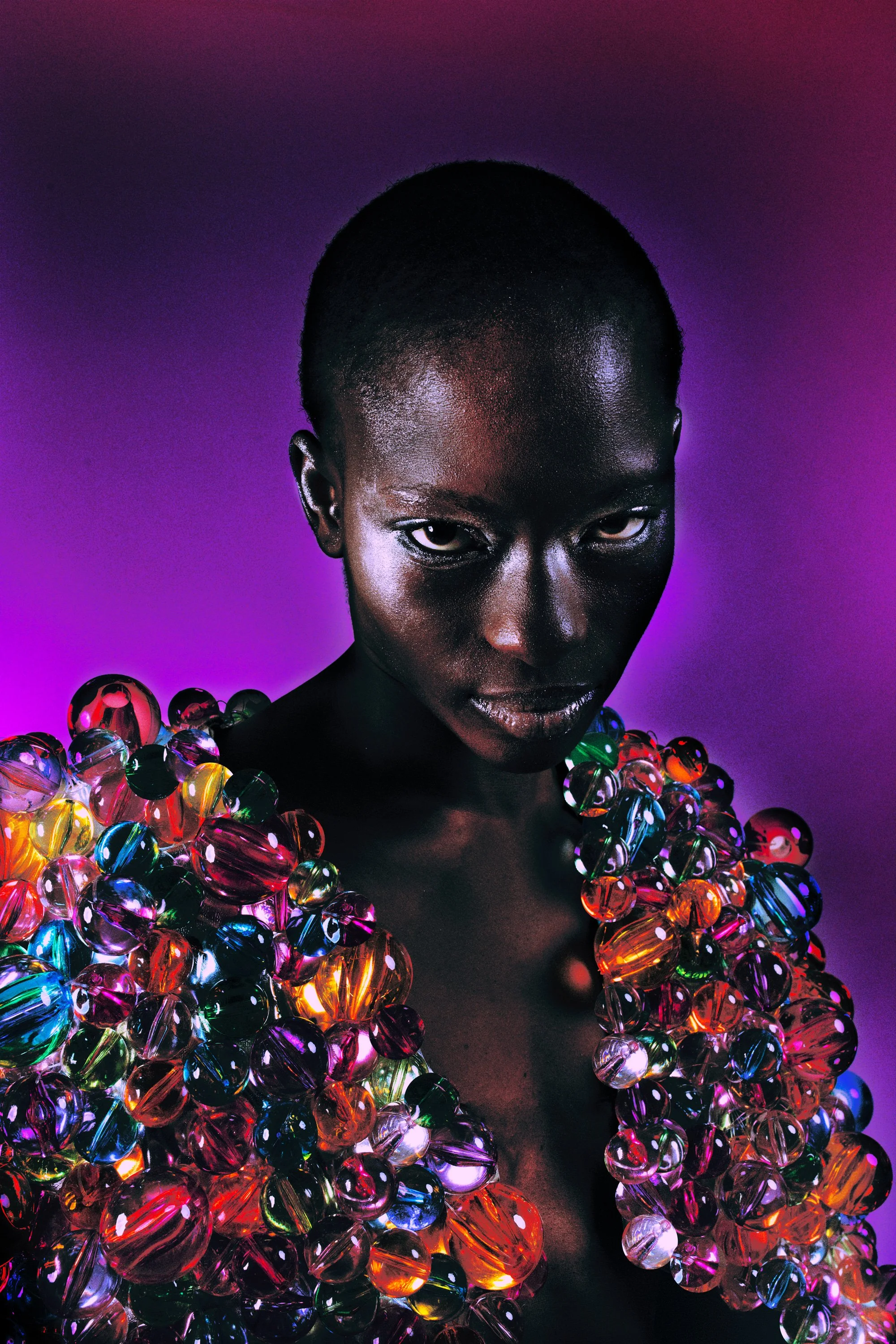 Portrait d'une femme noire avec une peau brillante, portant un vêtement décoré de nombreuses perles colorées, contre un fond violet dégradé.
