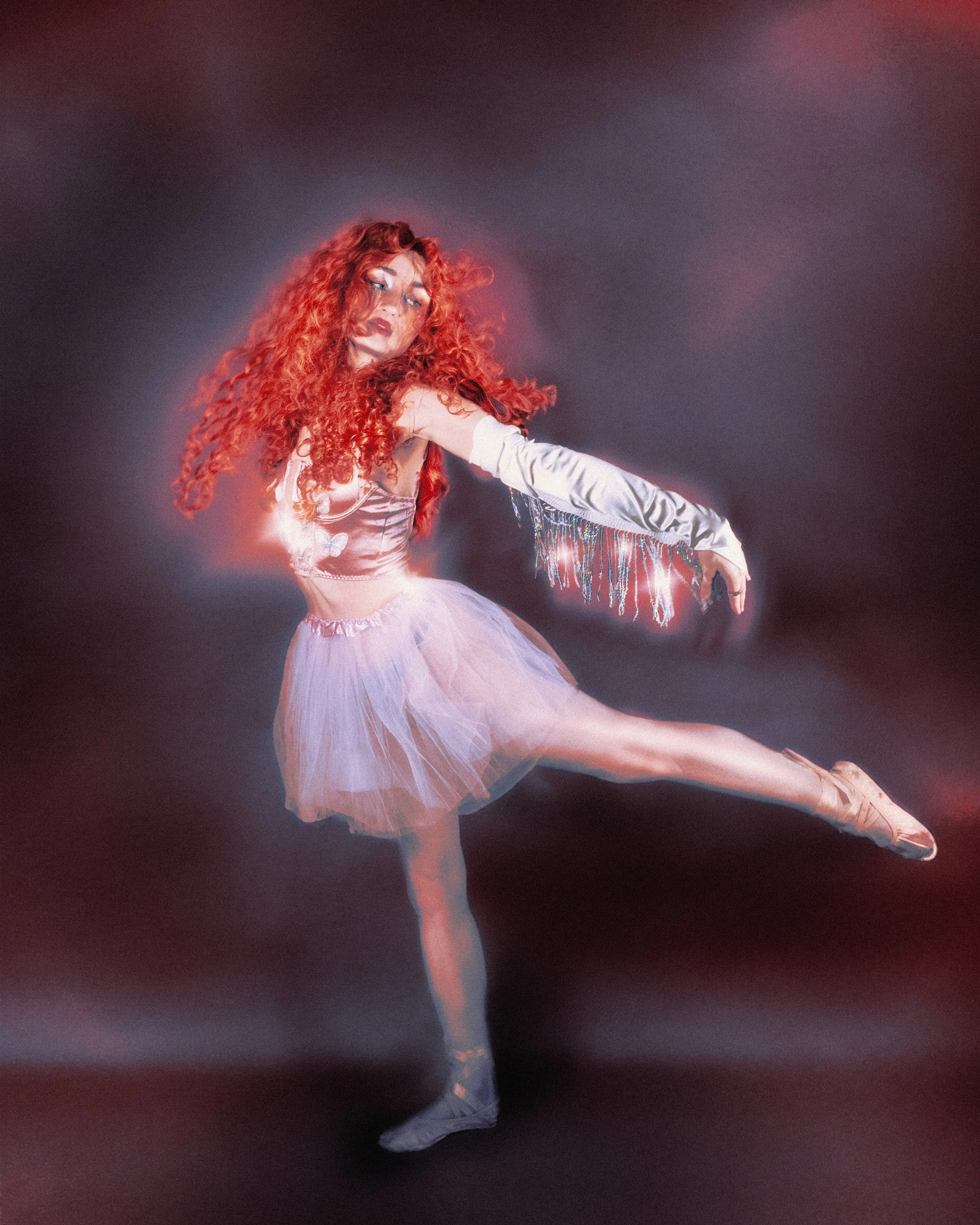 Danseuse de ballet en tutu rose, portant une robe argentée avec des franges et des gants long argentés, danse sur scène dans une pose élégante avec un fond sombre et lumineux.