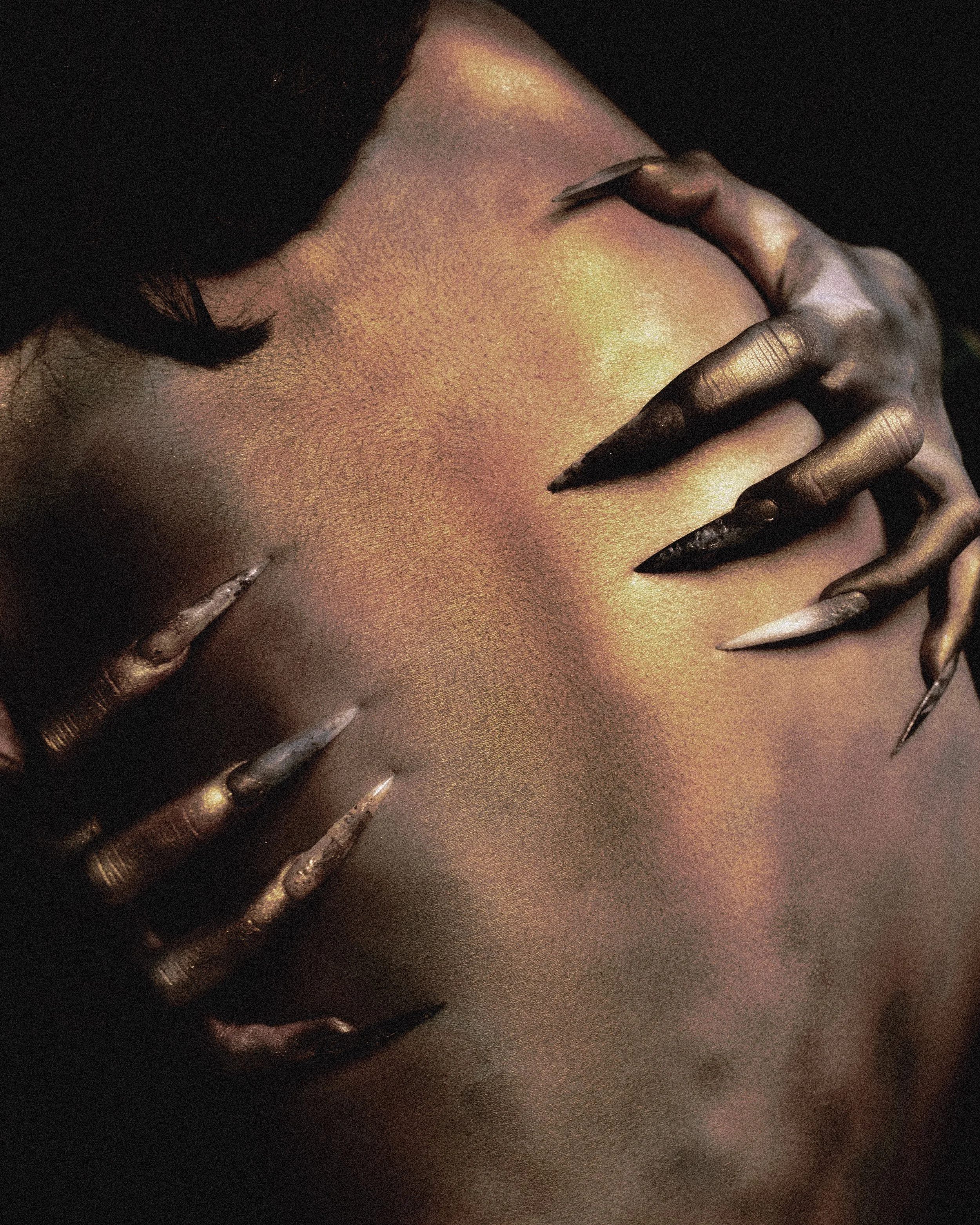 Une personne avec un maquillage doré et des ongles longs, pointus, en noir et blanc, touchant son visage dans un style artistique et glamour.