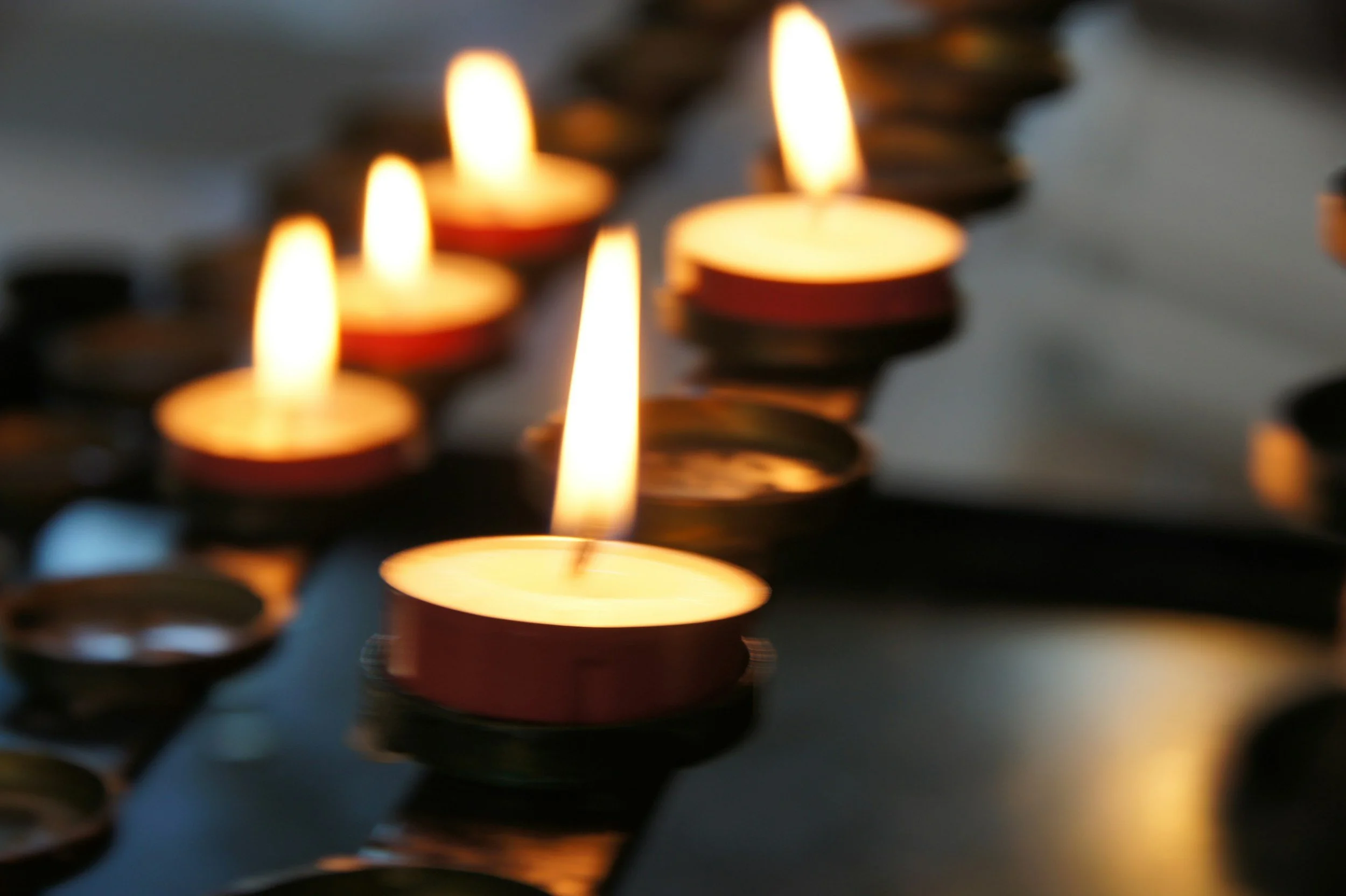 Multiple lit tealight candles placed on a reflective surface, creating a warm glow.