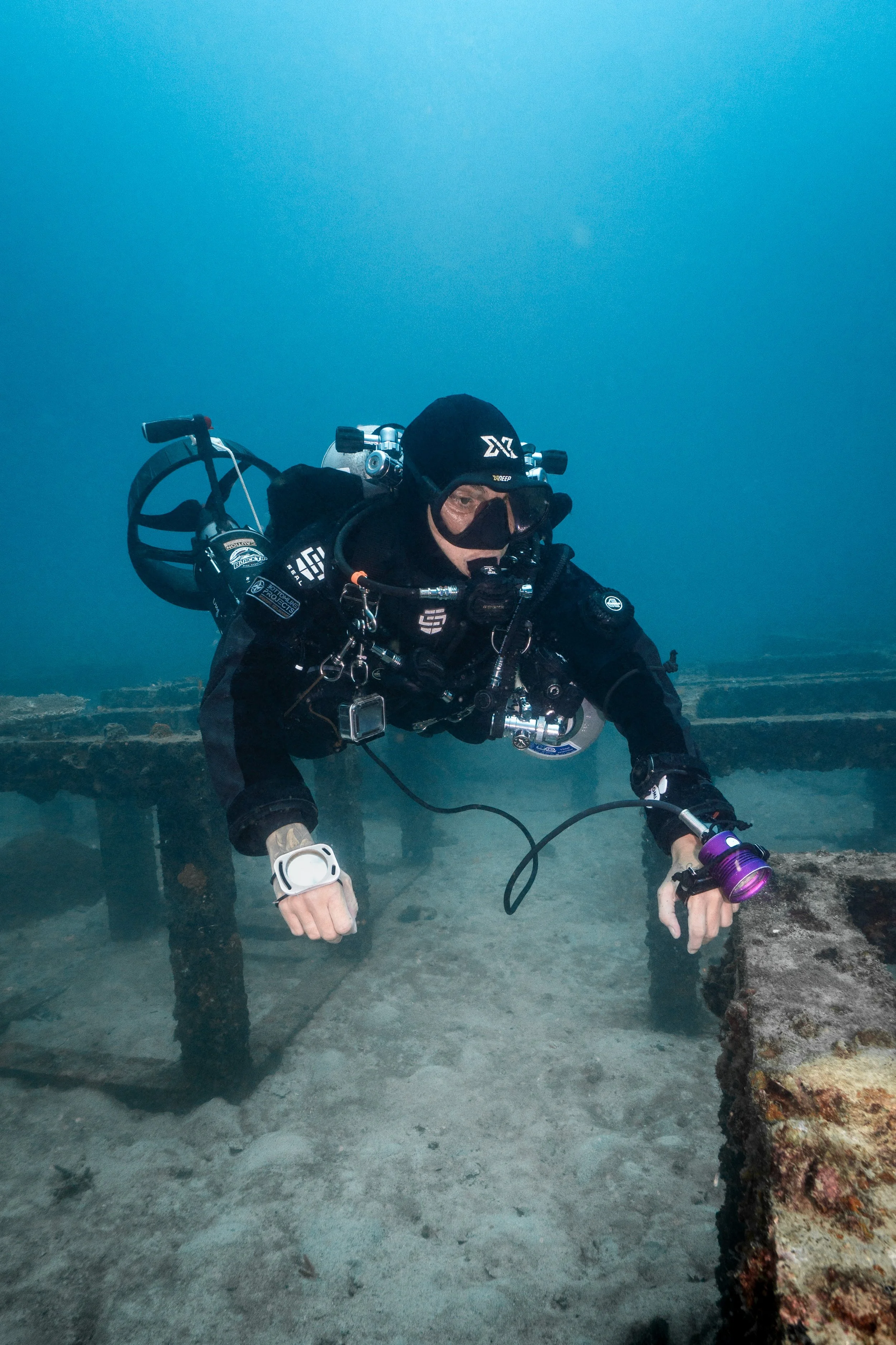 A scuba diver in black gear underwater near a shipwreck.