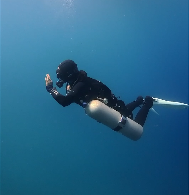 A diver wearing a black wetsuit, mask, and fins, swimming underwater with an oxygen tank and scuba gear.