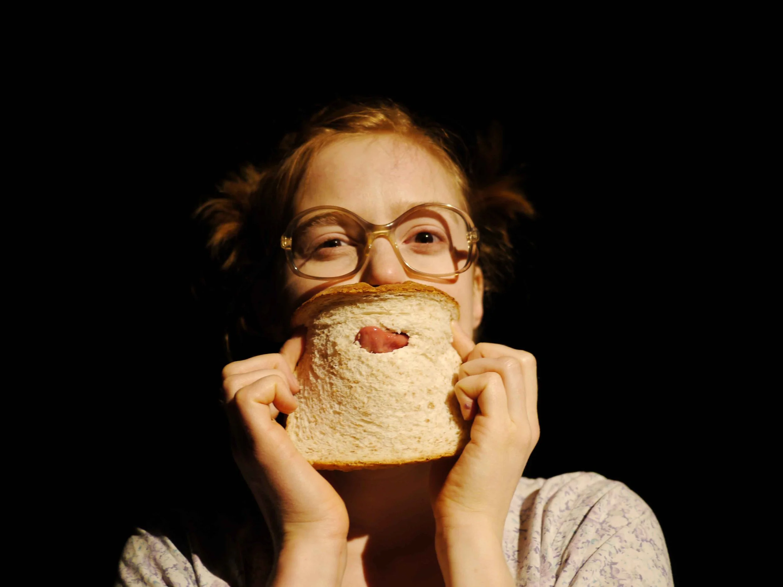 A picture of performer Ingrid Hansen sticking her tongue through a hole in a slice of bread