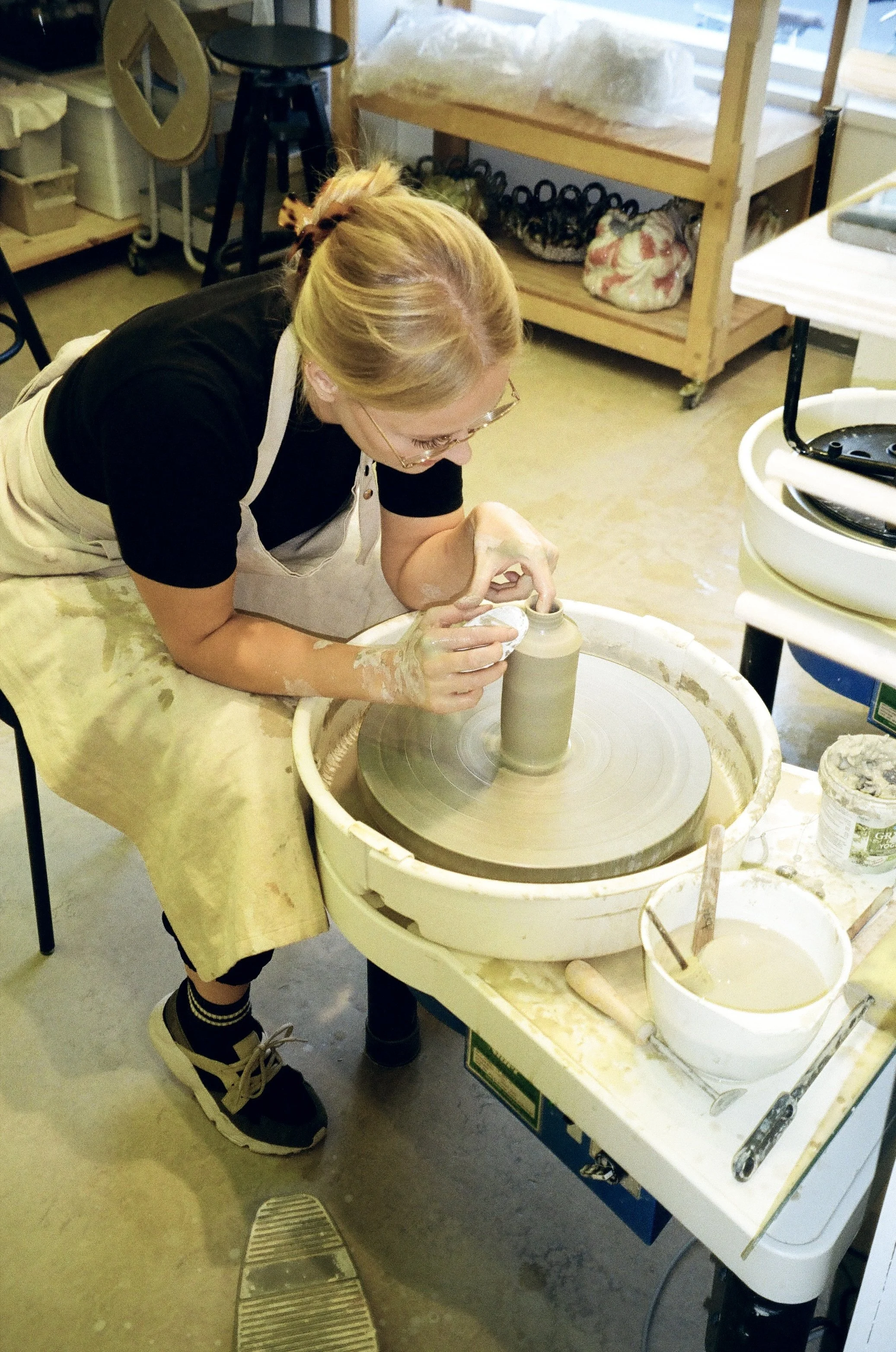 A woman working on a pottery wheel shaping clay into a vase in a ceramics studio.