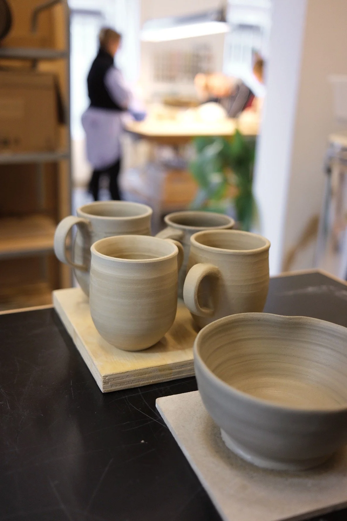 Unfinished ceramic mugs and bowls on a black surface in a pottery workshop.